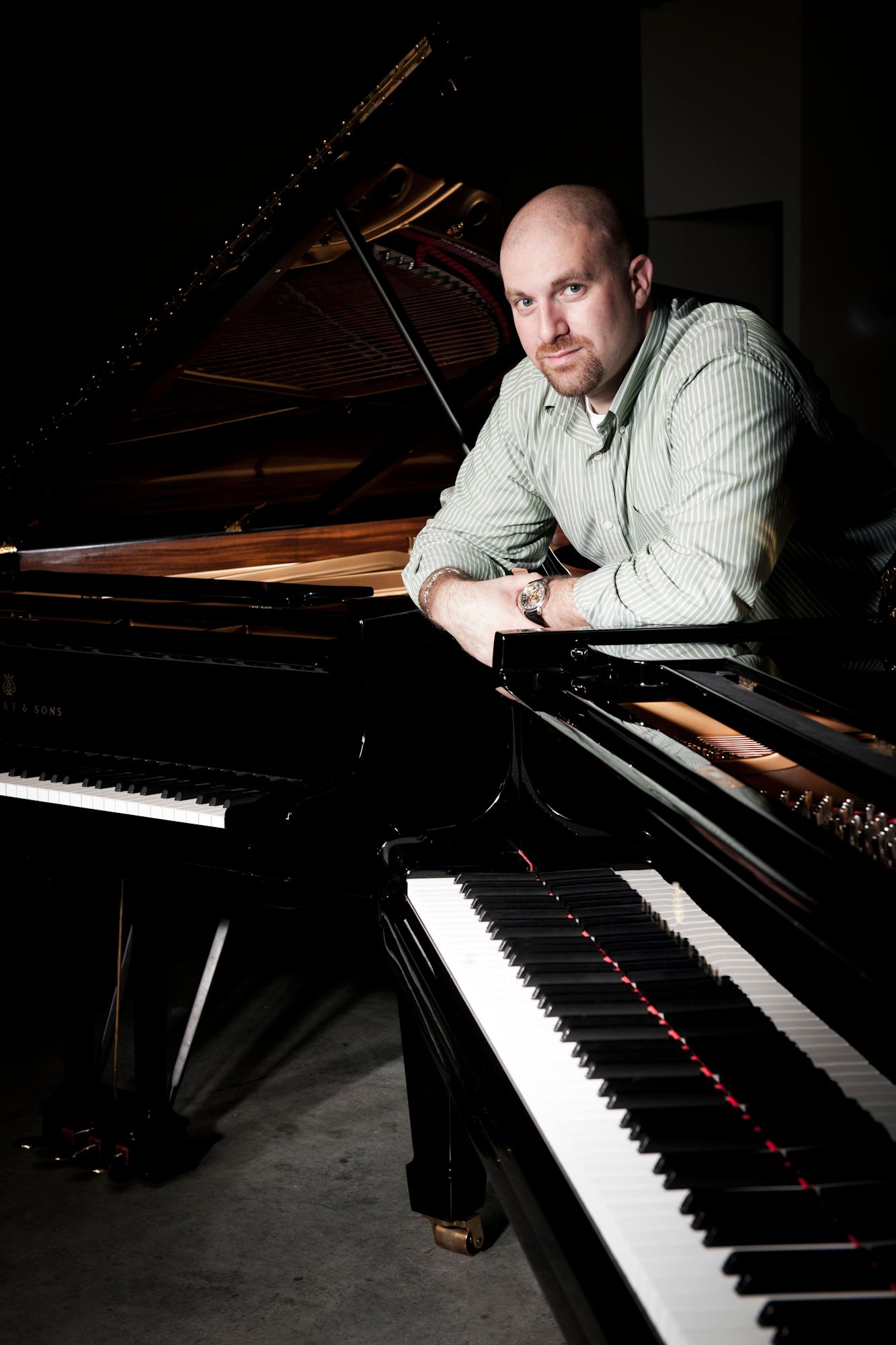 Musician leaning on grand piano in dramatic lighting. Commercial Photographer in Guelph Ontario