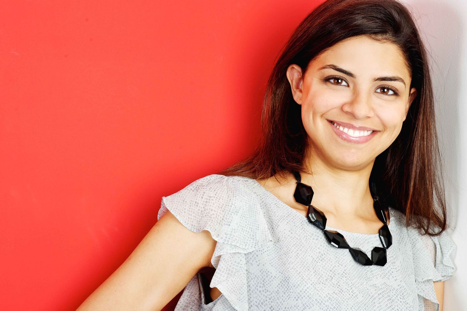 Woman in casual attire smiling against bright red background. Commercial Photographer in Guelph Ontario