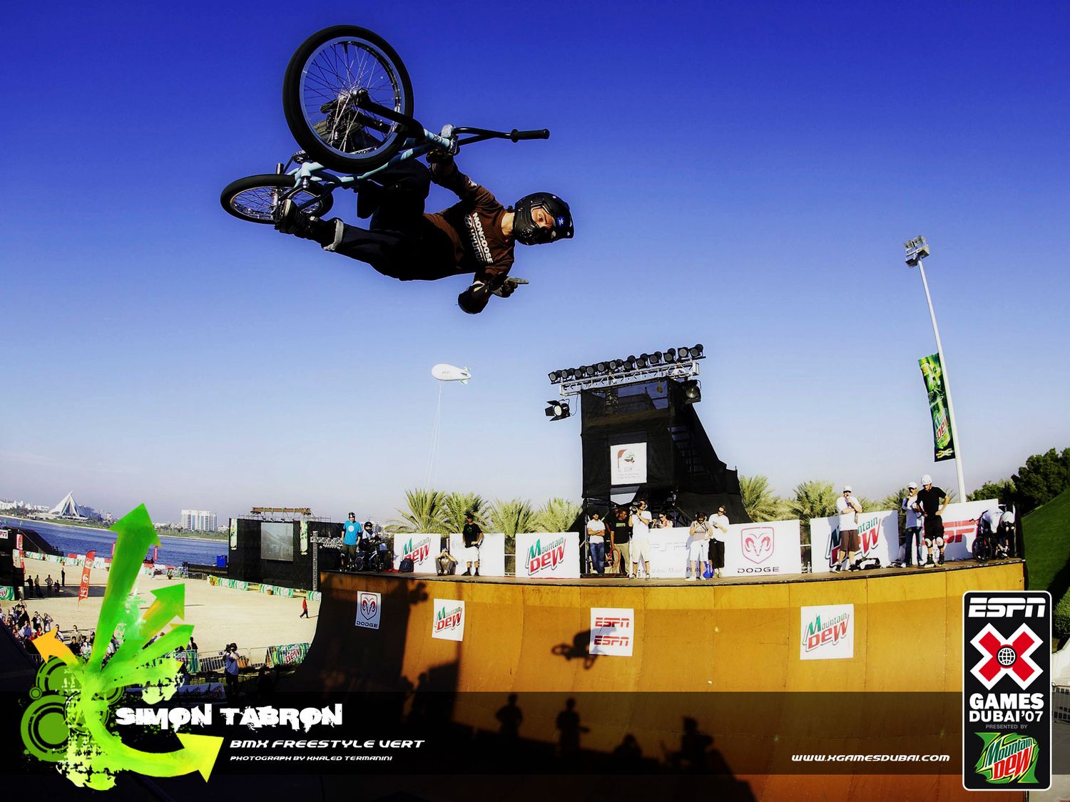 Extreme sports athletes performing BMX tricks against blue sky at outdoor competition.