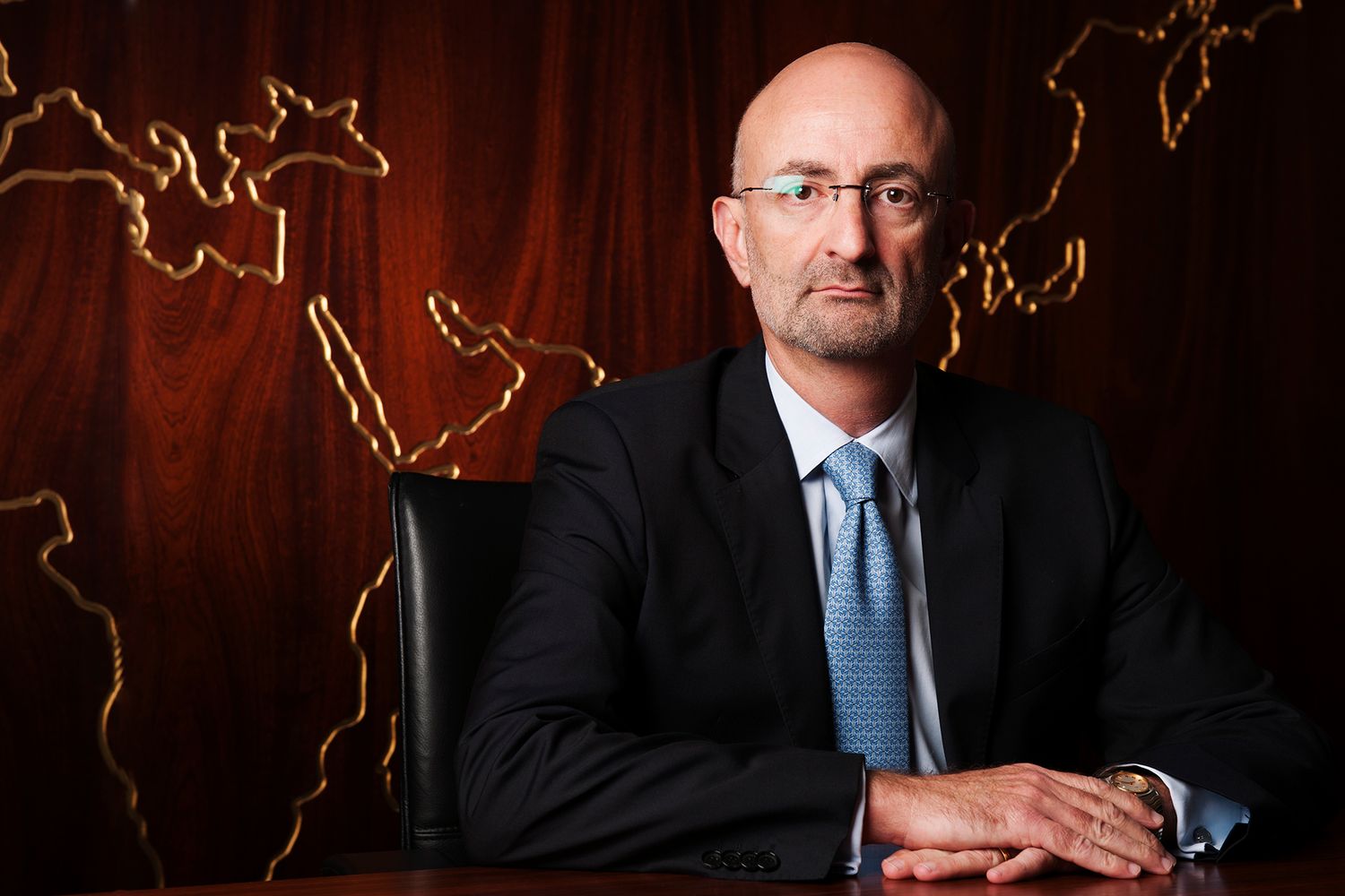 Executive seated at desk with illuminated world map on wood paneled wall behind. Commercial Portrait photographer in Ontario