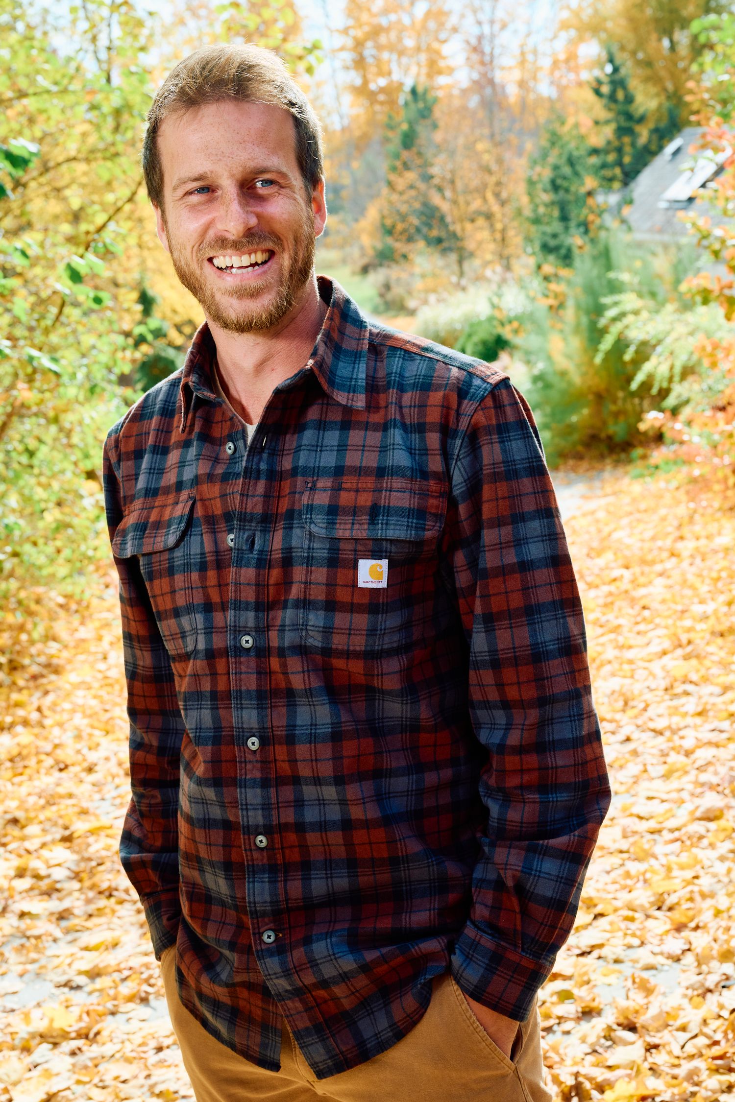 Person wearing plaid flannel shirt smiles outdoors among autumn foliage. Portrait Photographer in Ontario