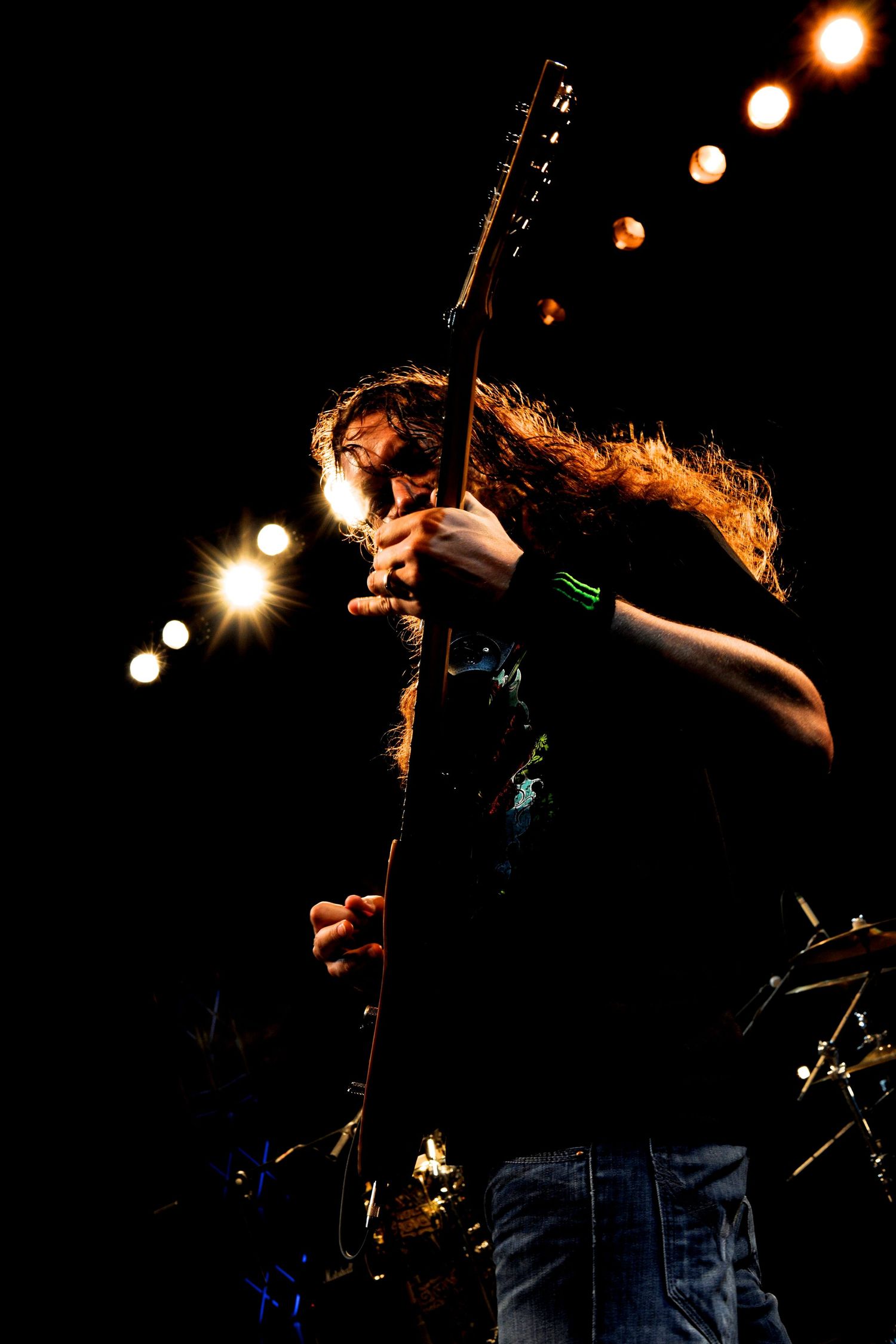 Rock musician performing on stage with dramatic lighting and hair movement during an energetic performance.