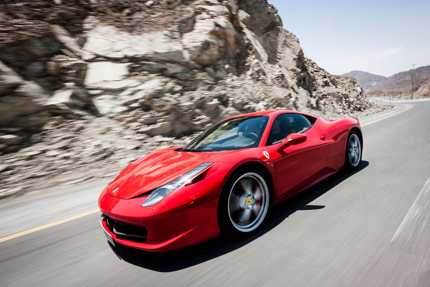 Red Ferrari sports car driving through winding mountain roads against dramatic rocky landscape. car photography in ontario