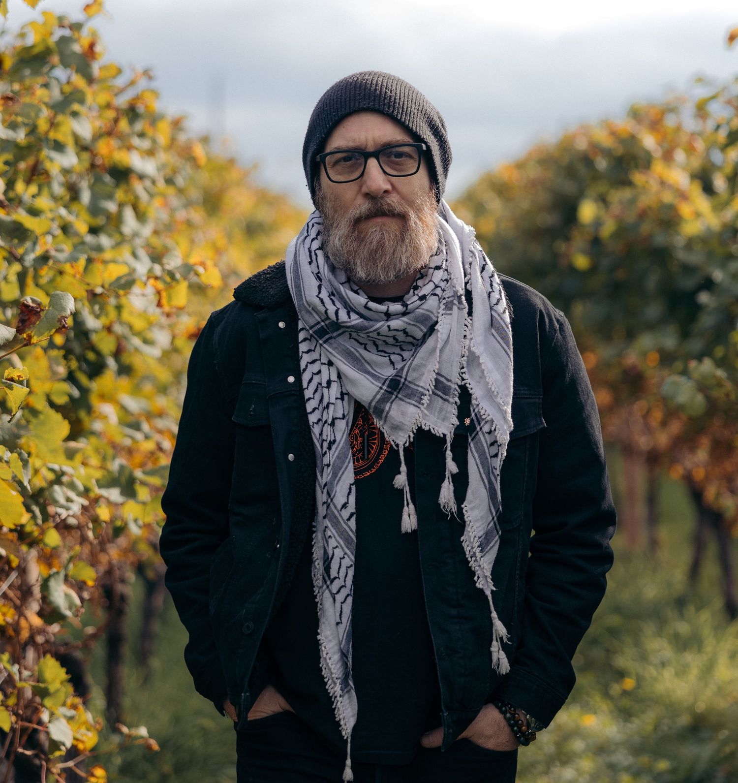 Person wearing winter accessories and glasses poses outdoors among autumn foliage.