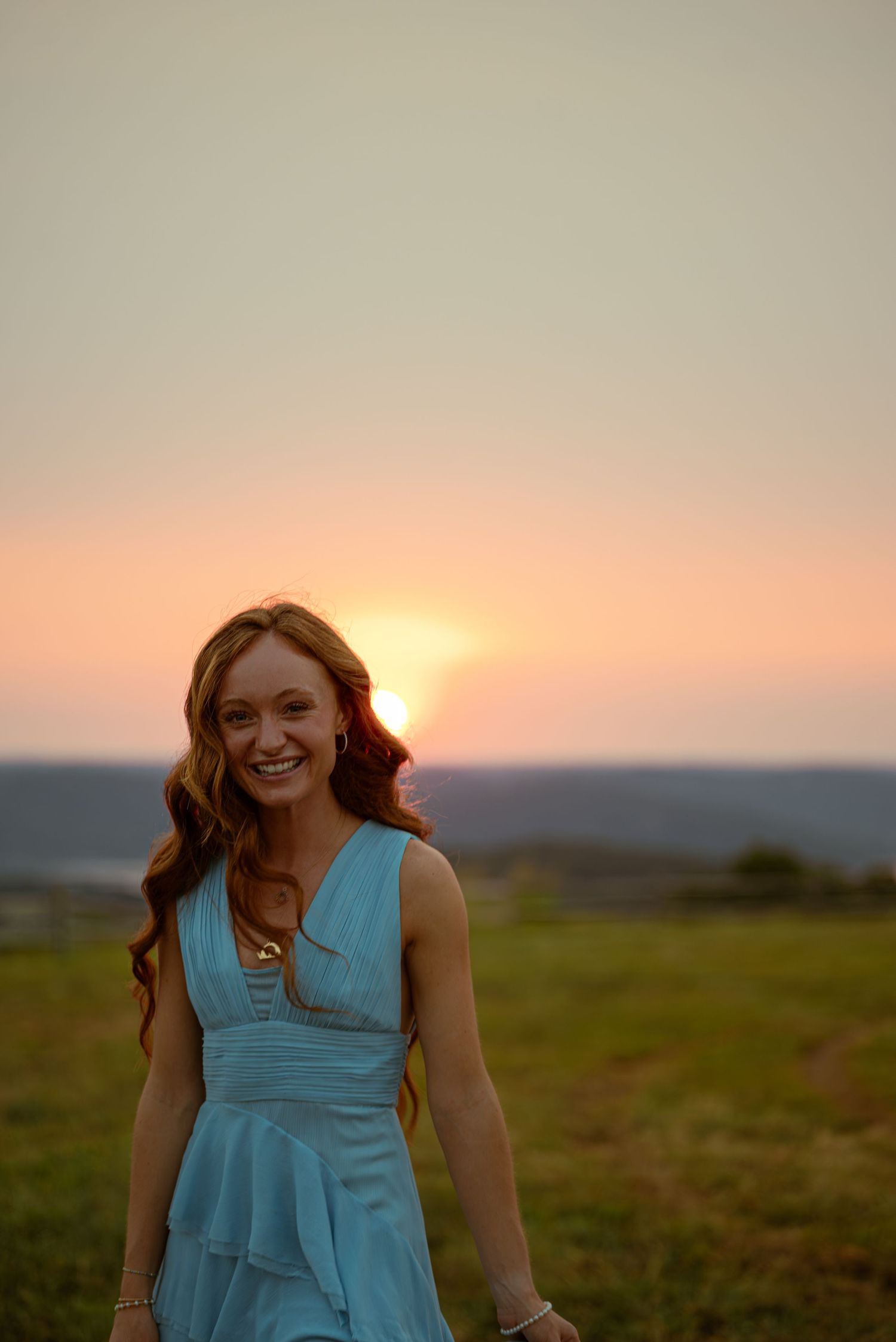 Happy redhead woman in light blue dress laughing outdoors during beautiful warm sunset.