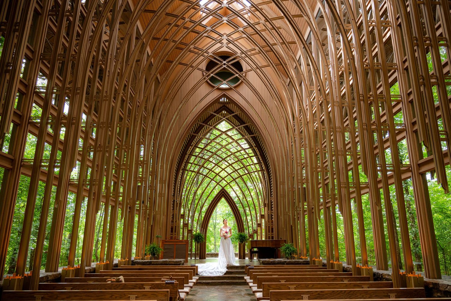 Stunning wooden chapel with Gothic arched ceiling, natural light, and a couple standing at the altar surrounded by lush greenery.