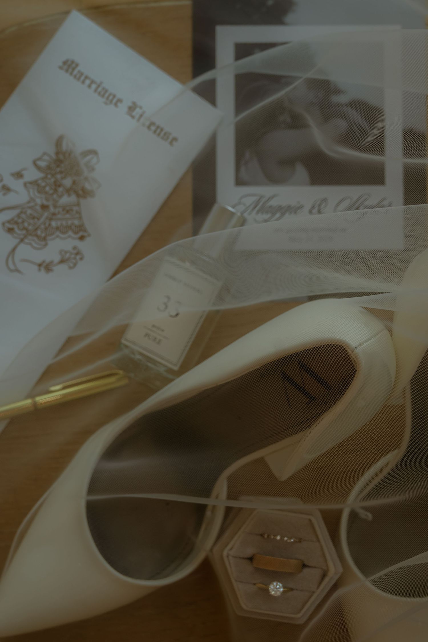 Wedding flat lay with marriage license, white heels, diamond ring, gold pen, and personalized photo card on wooden surface.