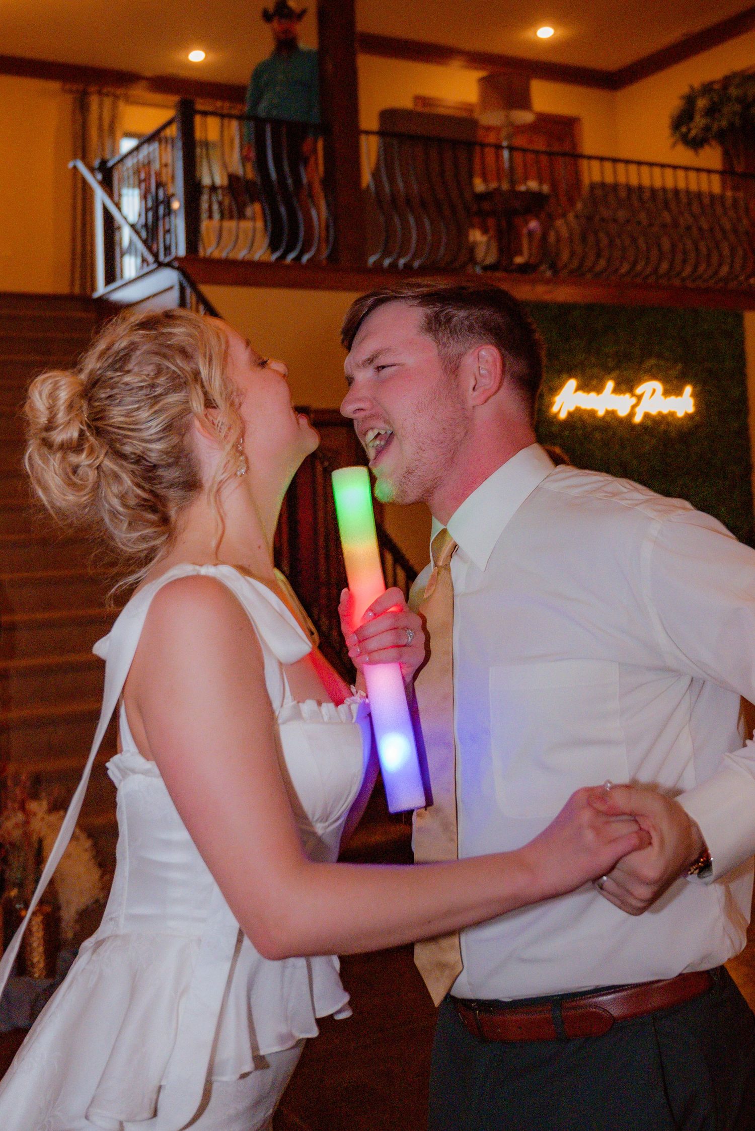 Bride and groom singing at each other during their reception, surrounded by lights and neon staffs.