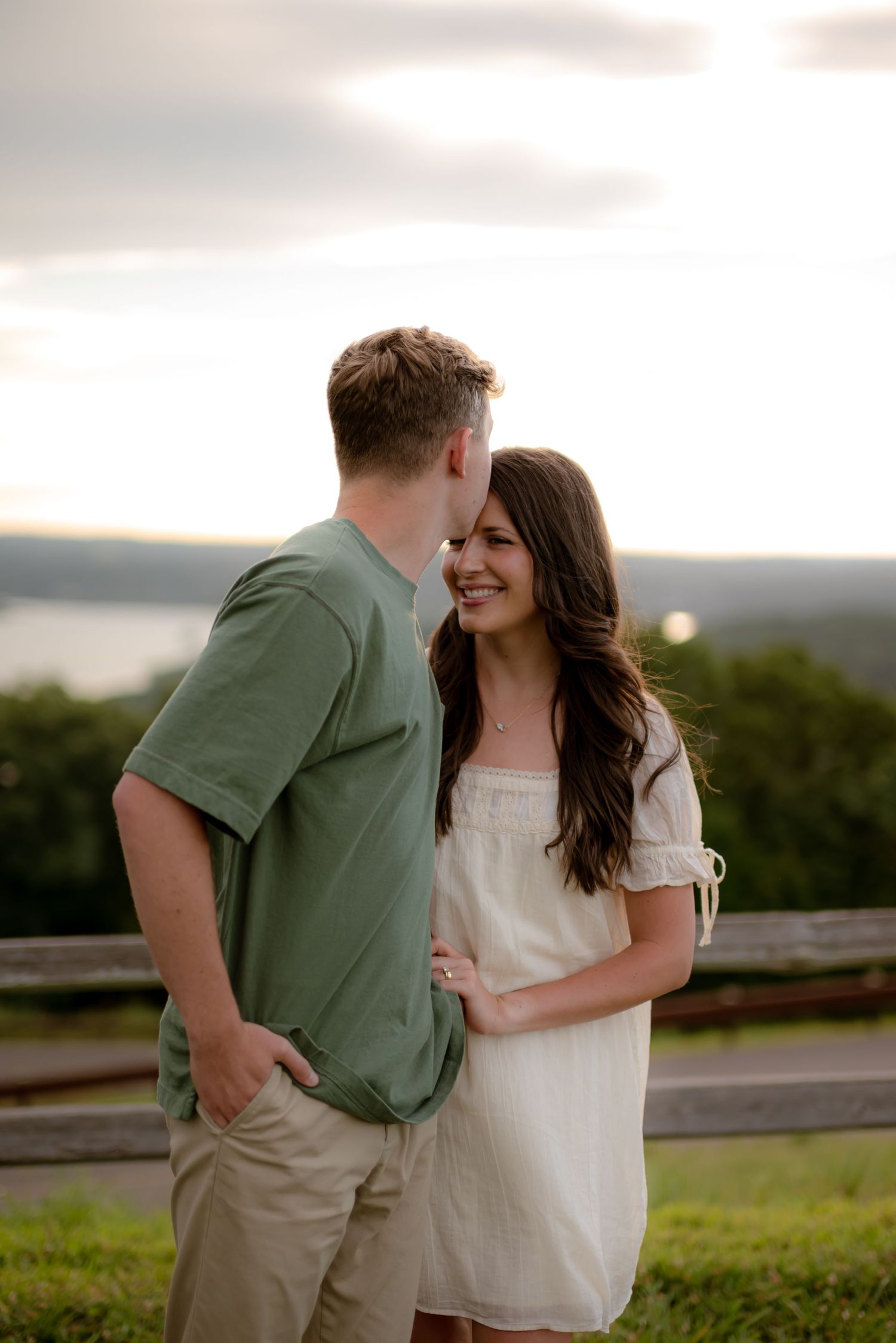 A couple shares a romantic moment outdoors at sunset, woman in white dress smiling at man in green shirt.