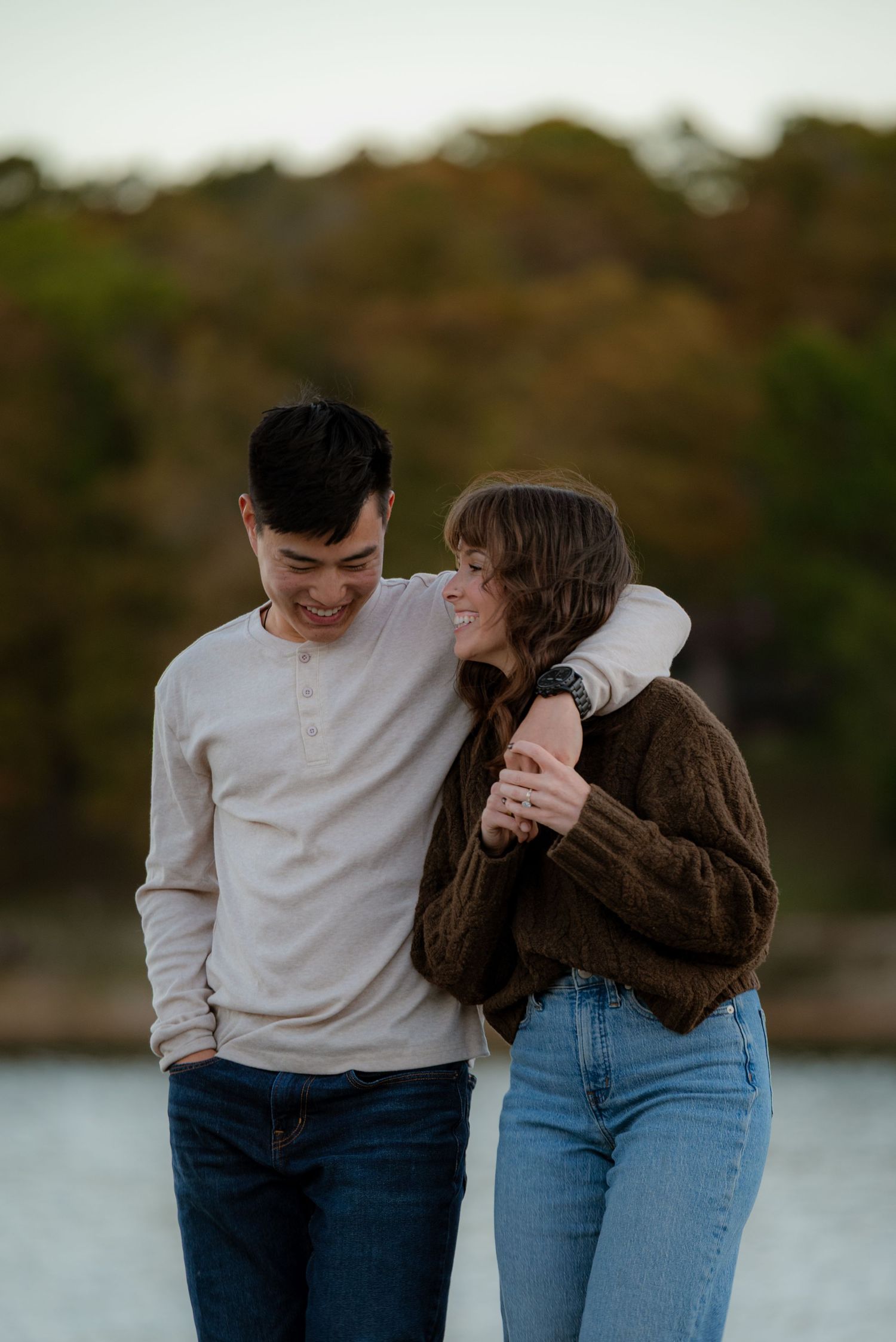 Happy couple laughing together near lakeside with autumn trees in soft background.