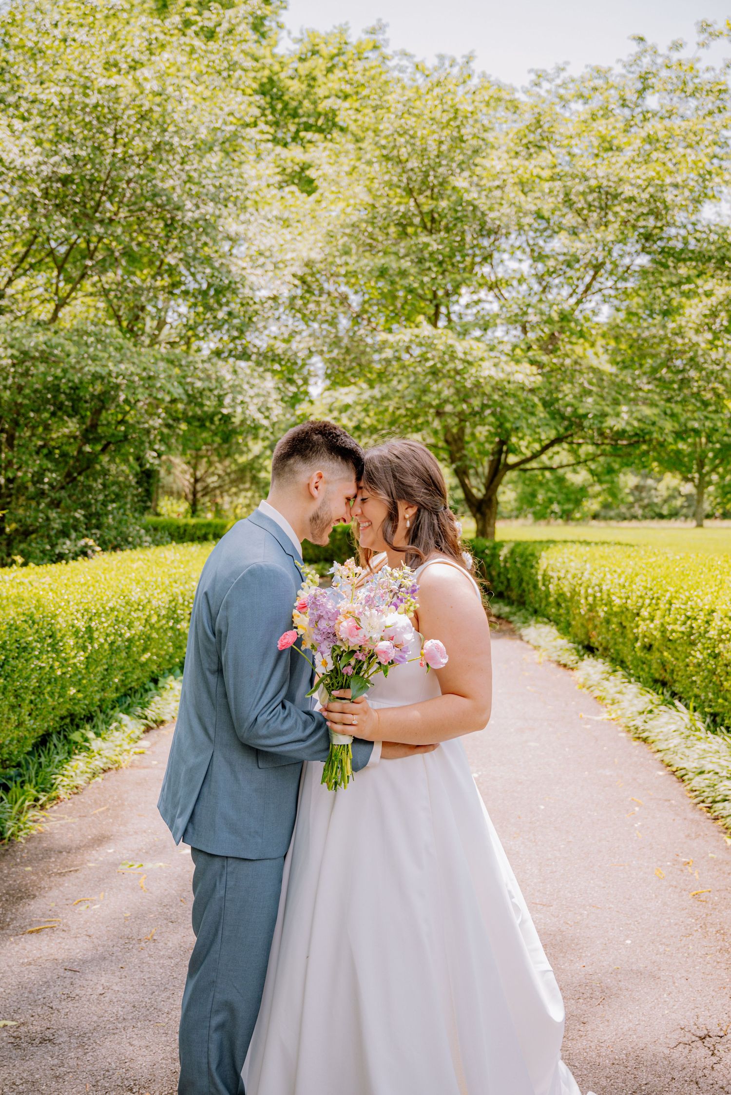 Bride and groom posing with their foreheads together as she hold her wedding flowers. They are on a beautiful outdoor walkway.