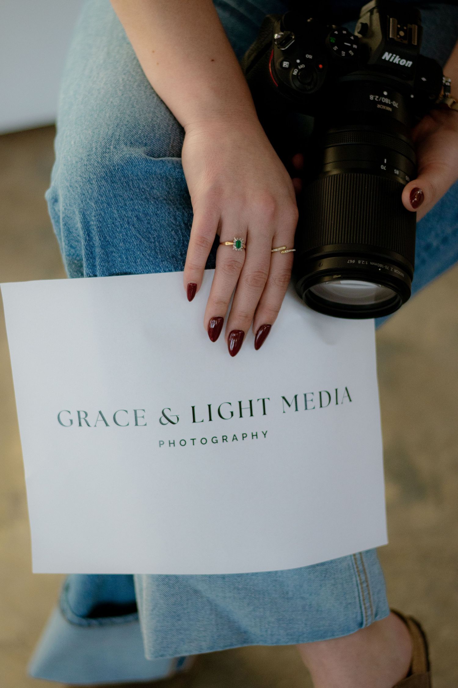 Woman holding Nikon camera and Grace and Light Media Photography branding card with red manicured nails.