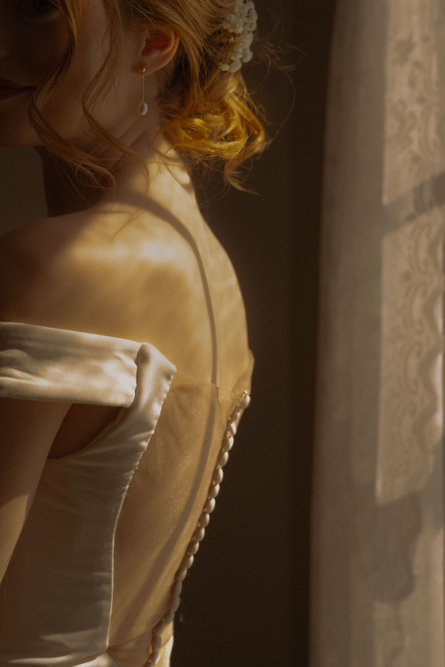 The back of a beautiful wedding dress on a bride surrounded by the light of a window.