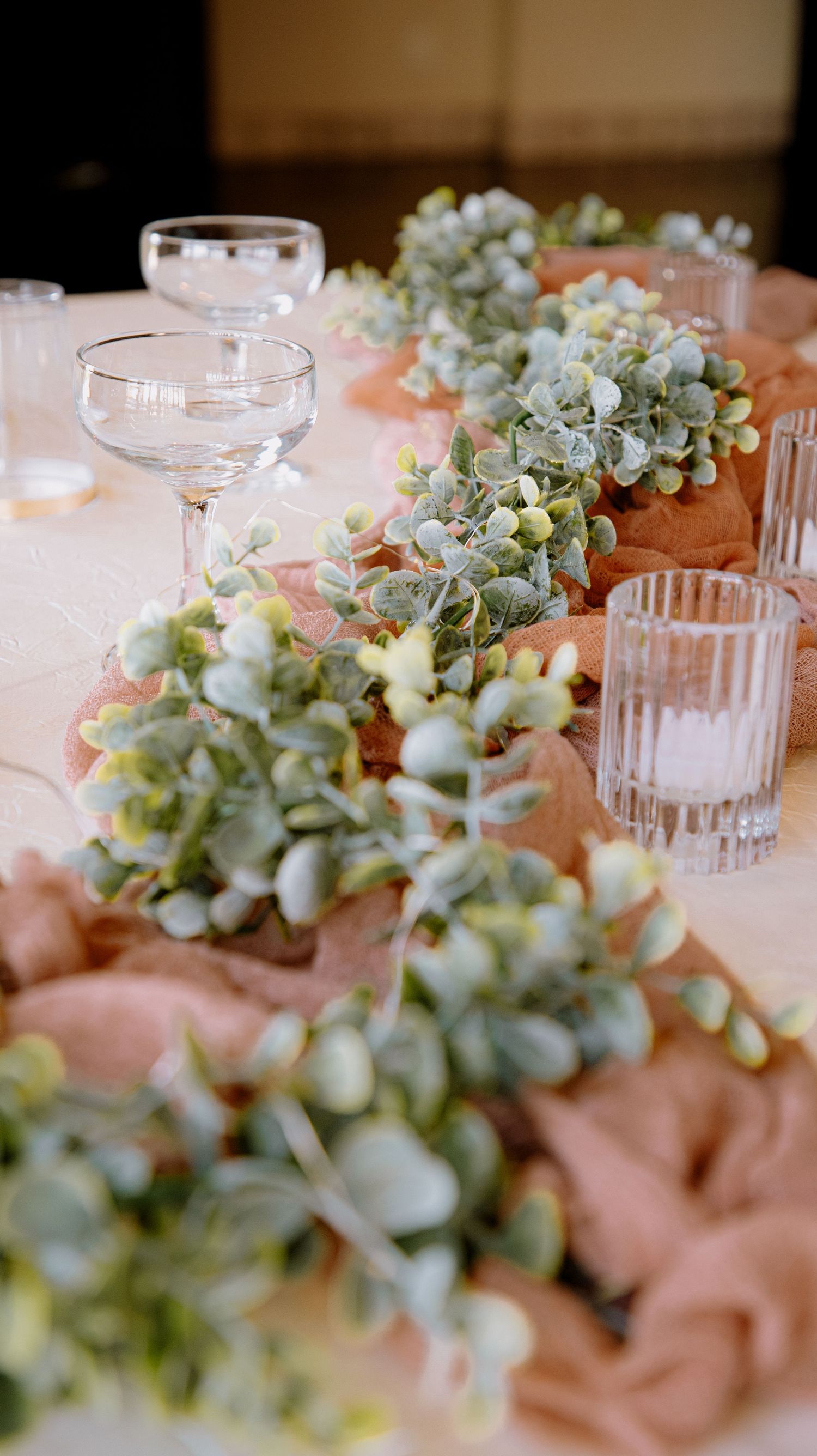Elegant wedding table centerpiece with eucalyptus garland, blush tulle runner, and crystal glassware.