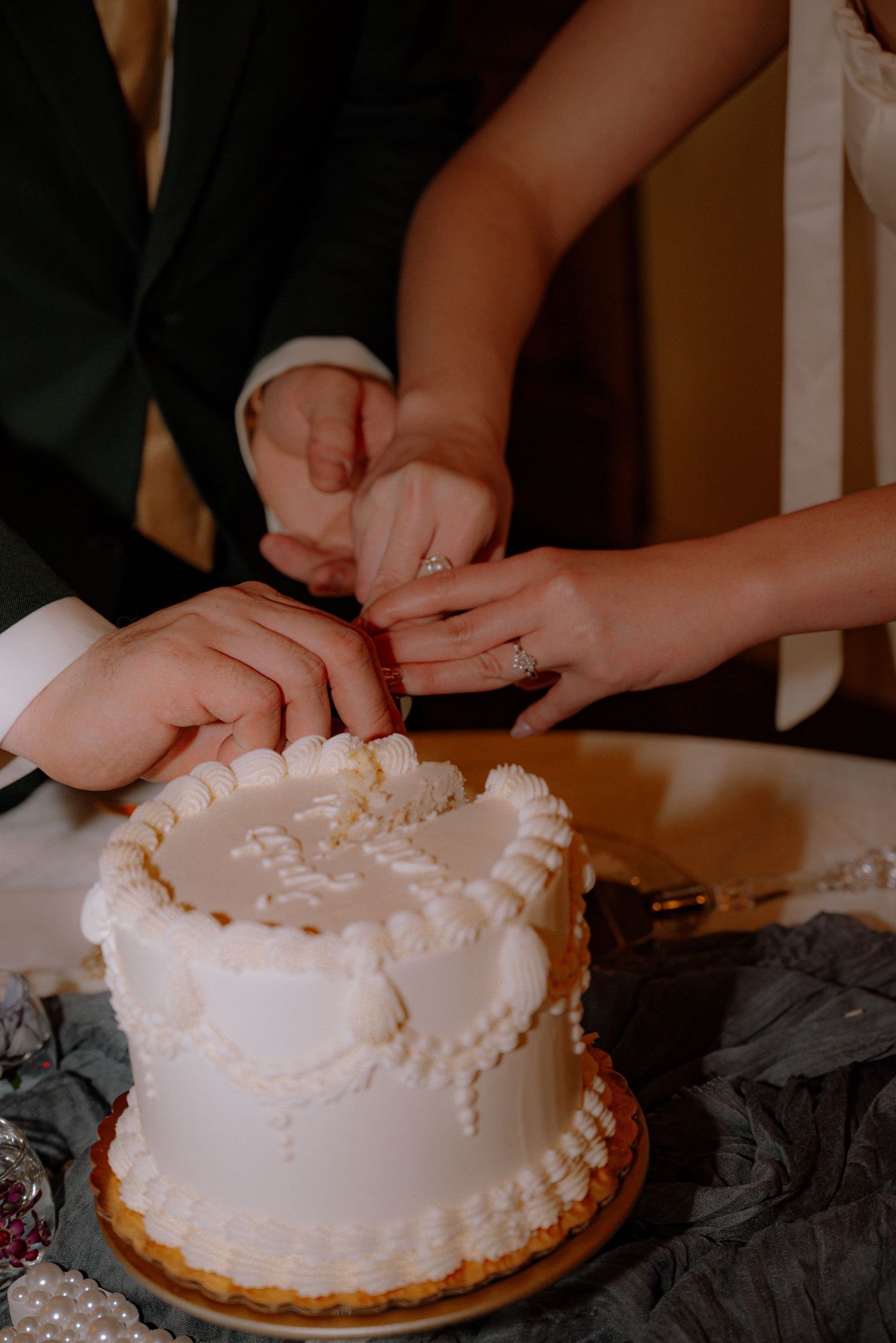 Bride and groom cutting their small white cake, surrounded by pearls and florals.