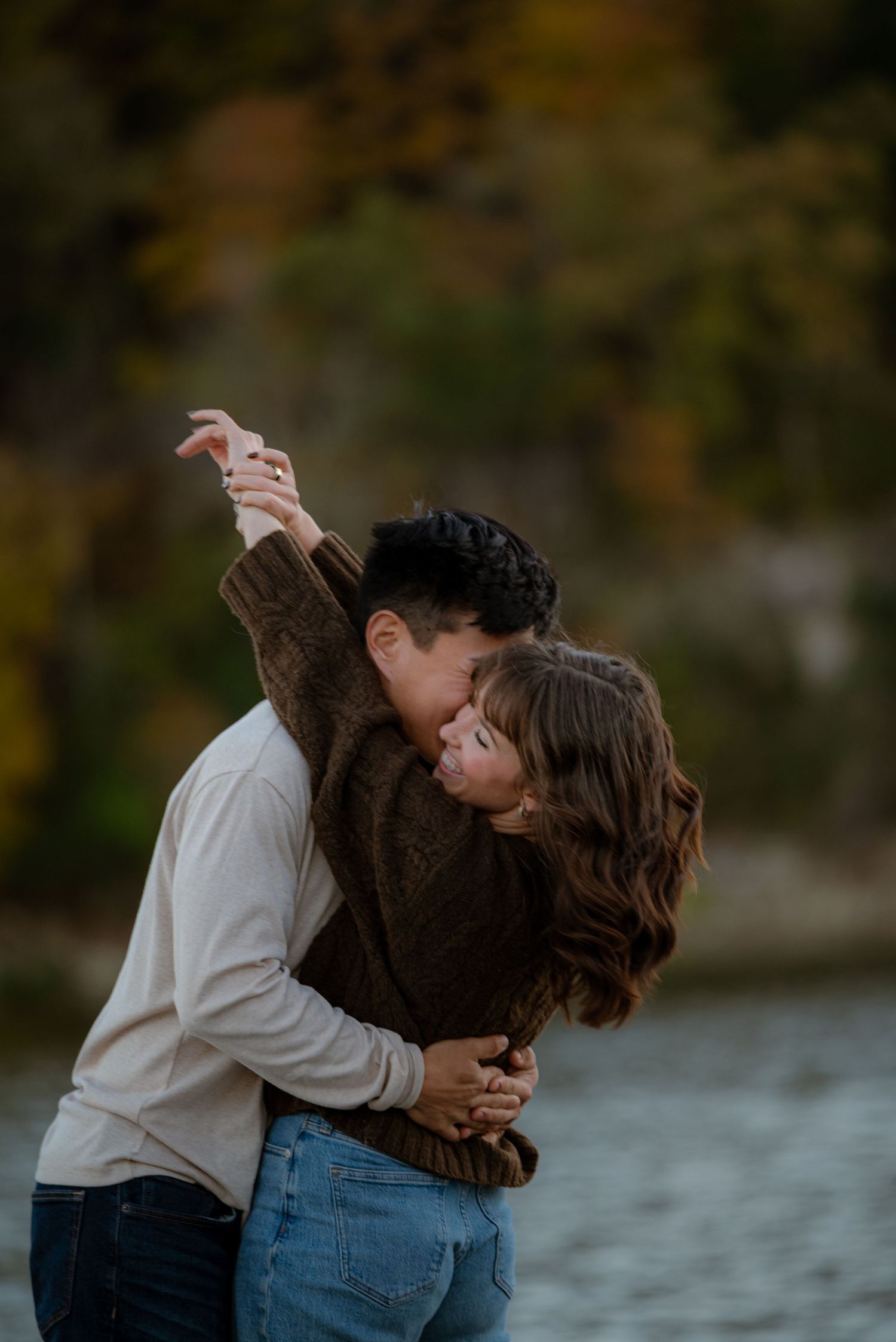 Couple sharing romantic dip kiss near autumn lake with colorful foliage background.