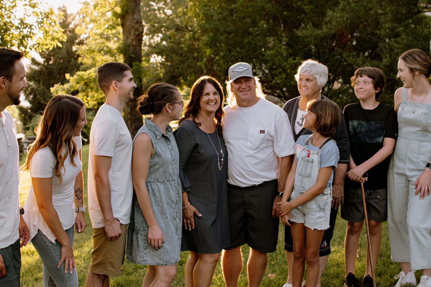 Large multigenerational family gathers together smiling outdoors in warm golden evening light.