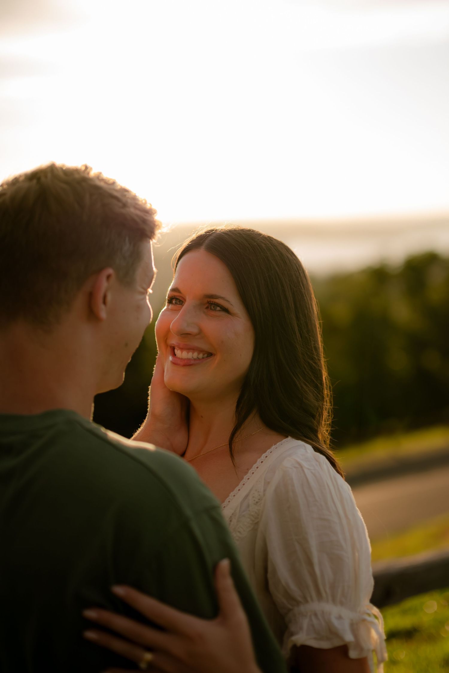 A couple shares a romantic sunset moment, the woman smiling warmly as the man gently cups her face outdoors.