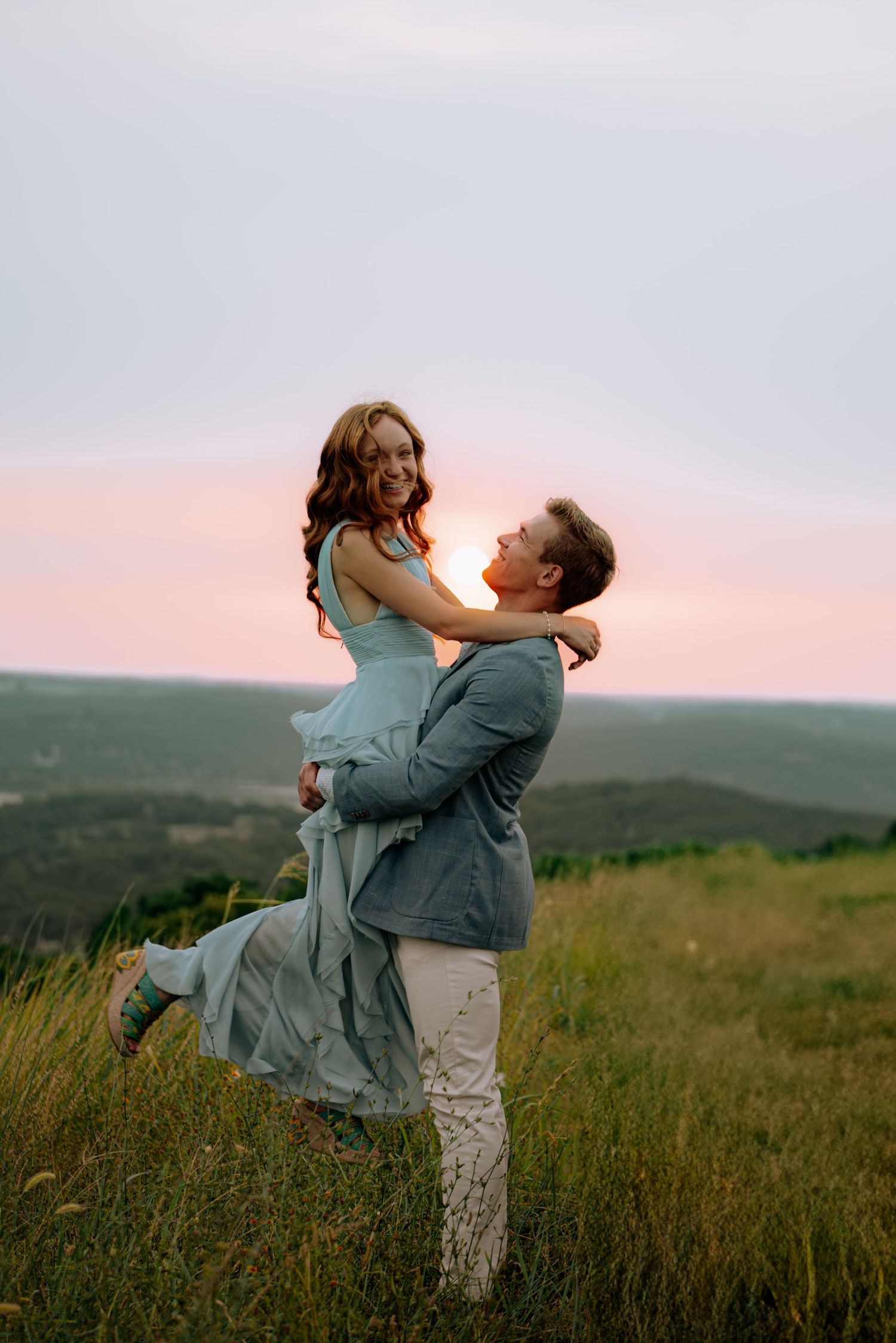 Couple embracing while he lifts her up in front of a sunset view.