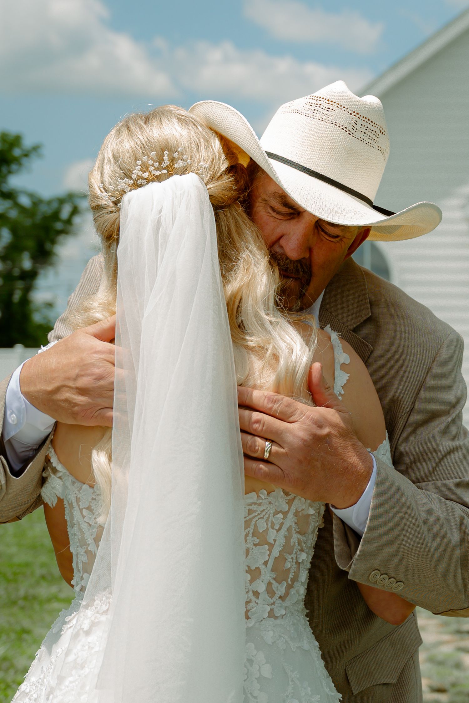 Bride's father embracing his daughter as he wears a cowboy hat outside.