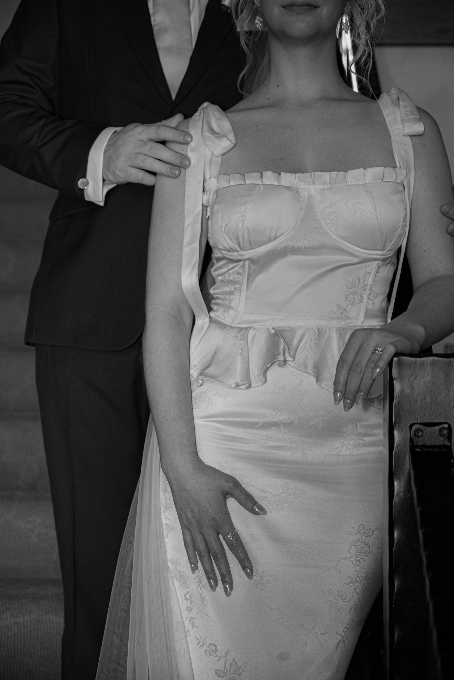 Black and white close-up of bride in corset wedding gown with groom placing hands on her shoulders.
