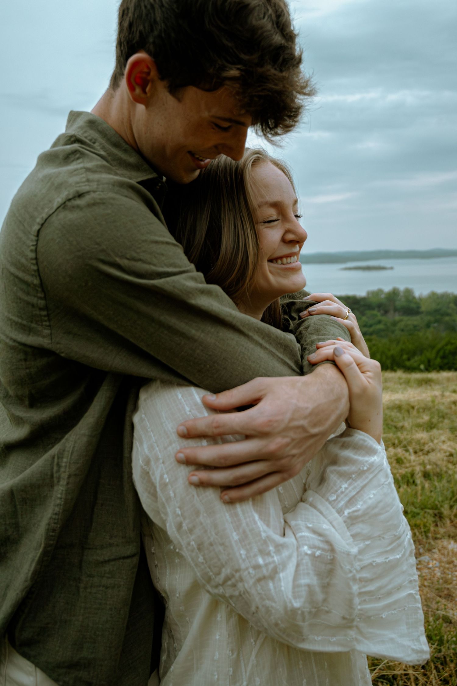 Couple posing for a photo while they laugh and embrace in front of a beautiful view.