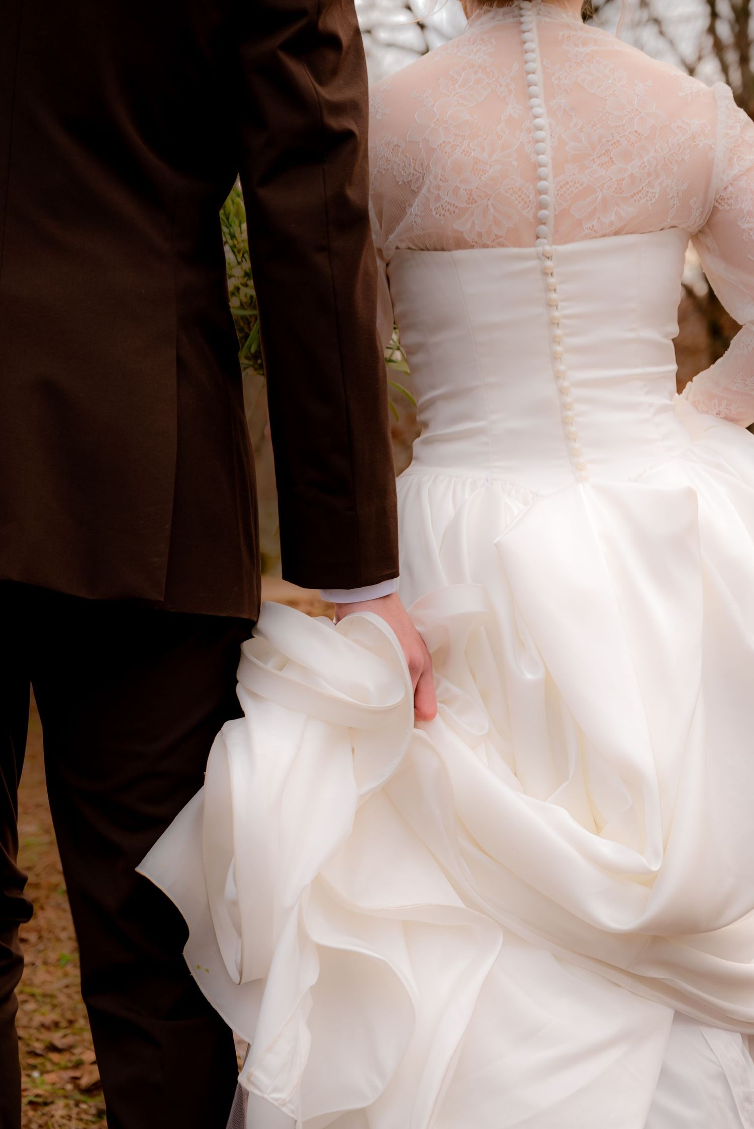 Close-up of bride and groom holding hands, showcasing lace back wedding gown with button detail.