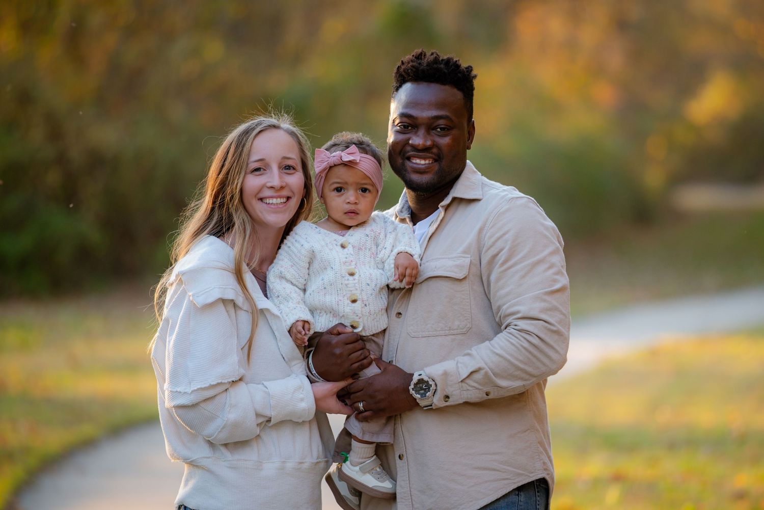 Smiling interracial family posing with their baby girl in a fall park setting.