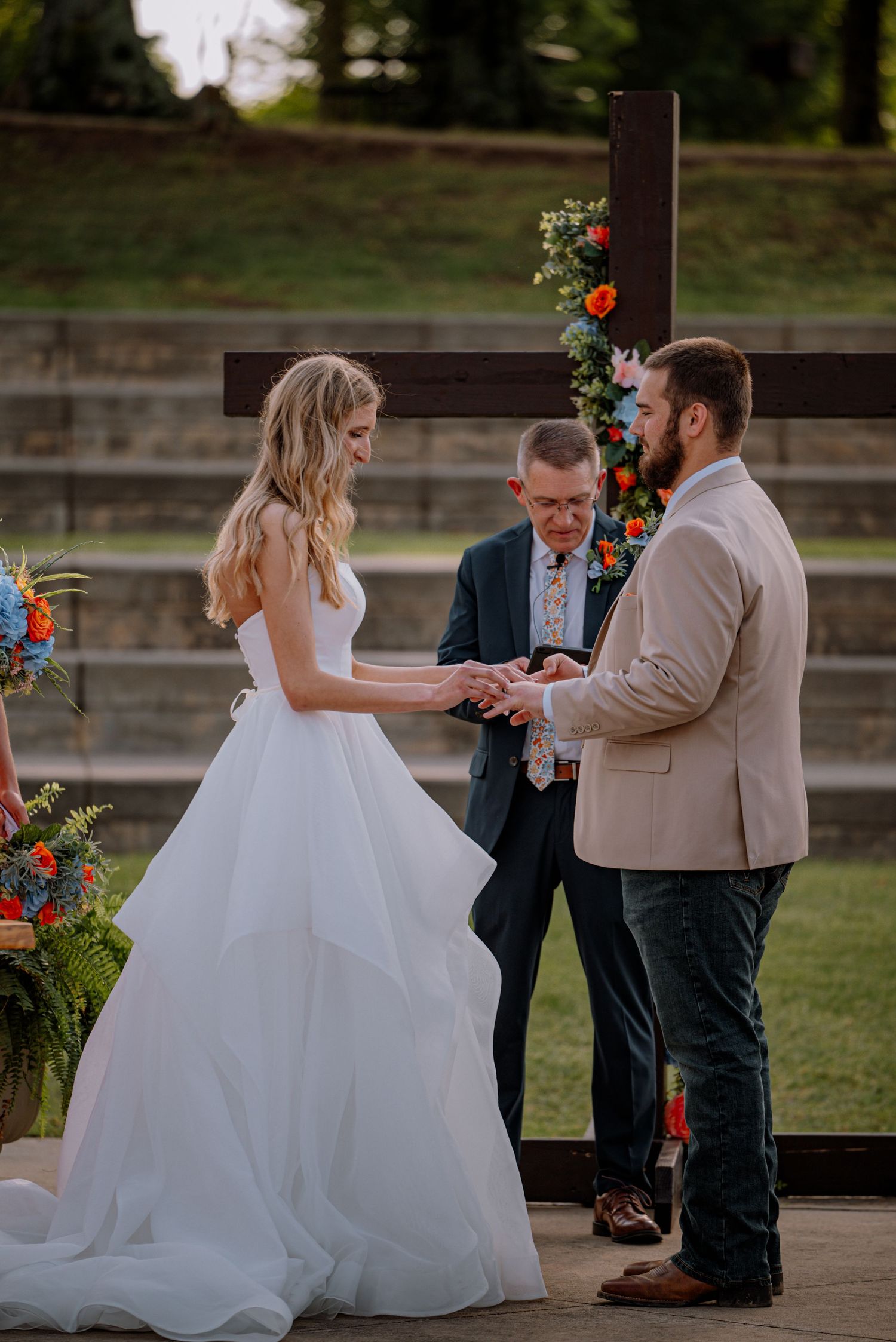 Bride and groom taking vows at the alter, surrounded by flowers and a cross.