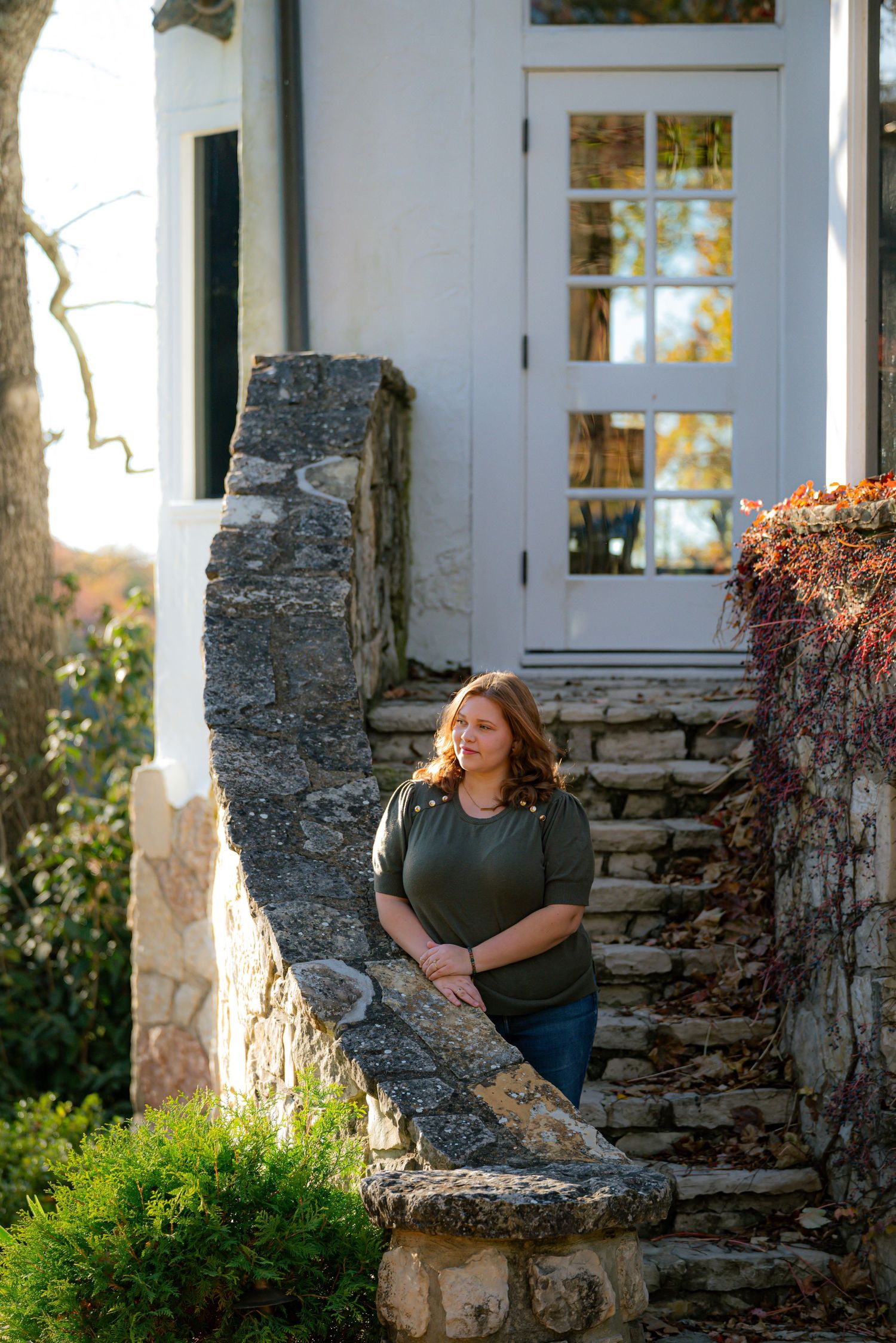 Woman in olive green top leaning on stone staircase railing outside a white historic building.