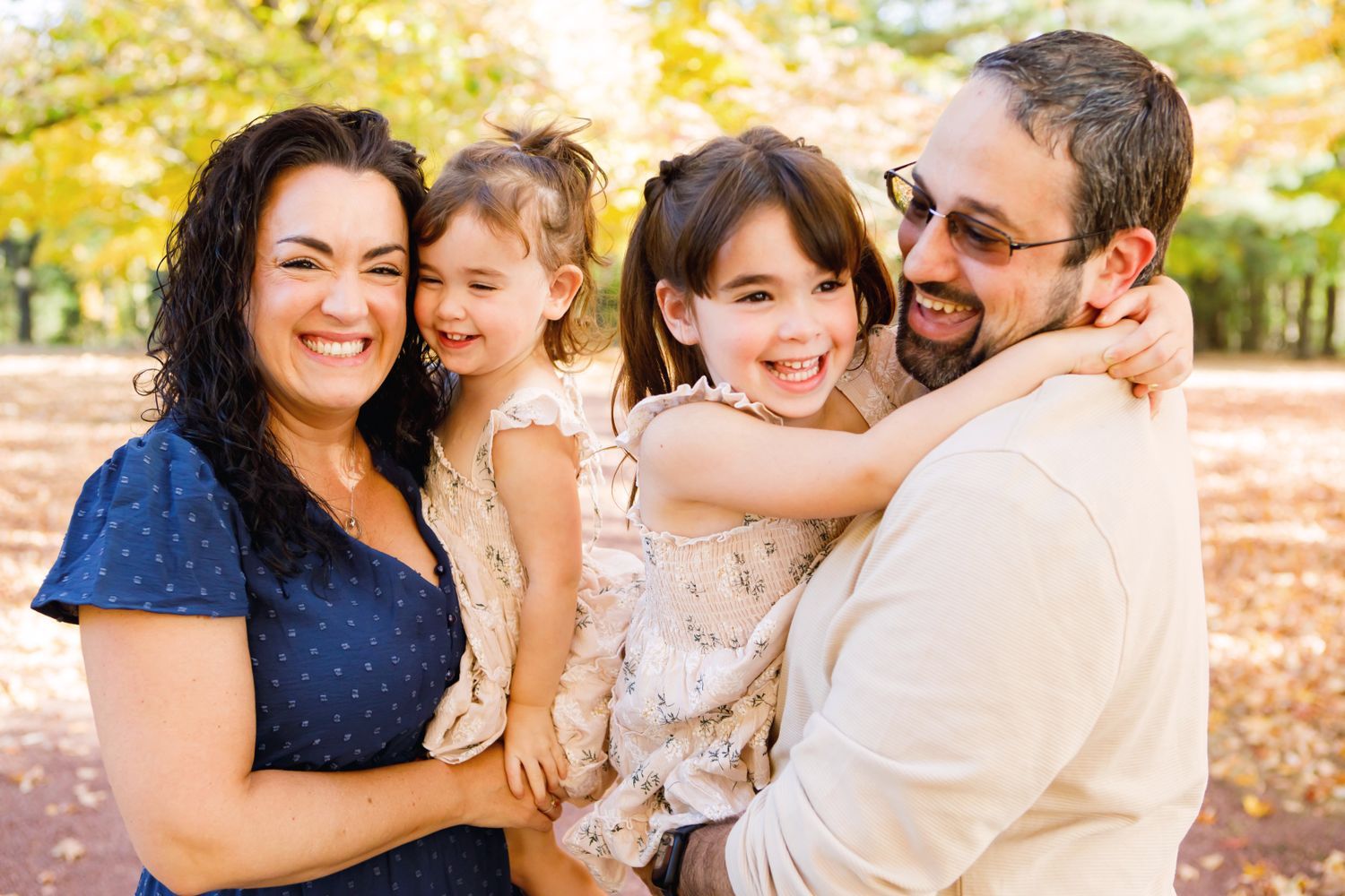 Joyful family of four laughing together in a colorful autumn park.