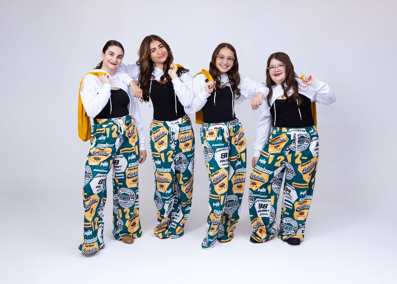 Four girls in colorful printed wide-leg pants and black tops pose together in a studio.