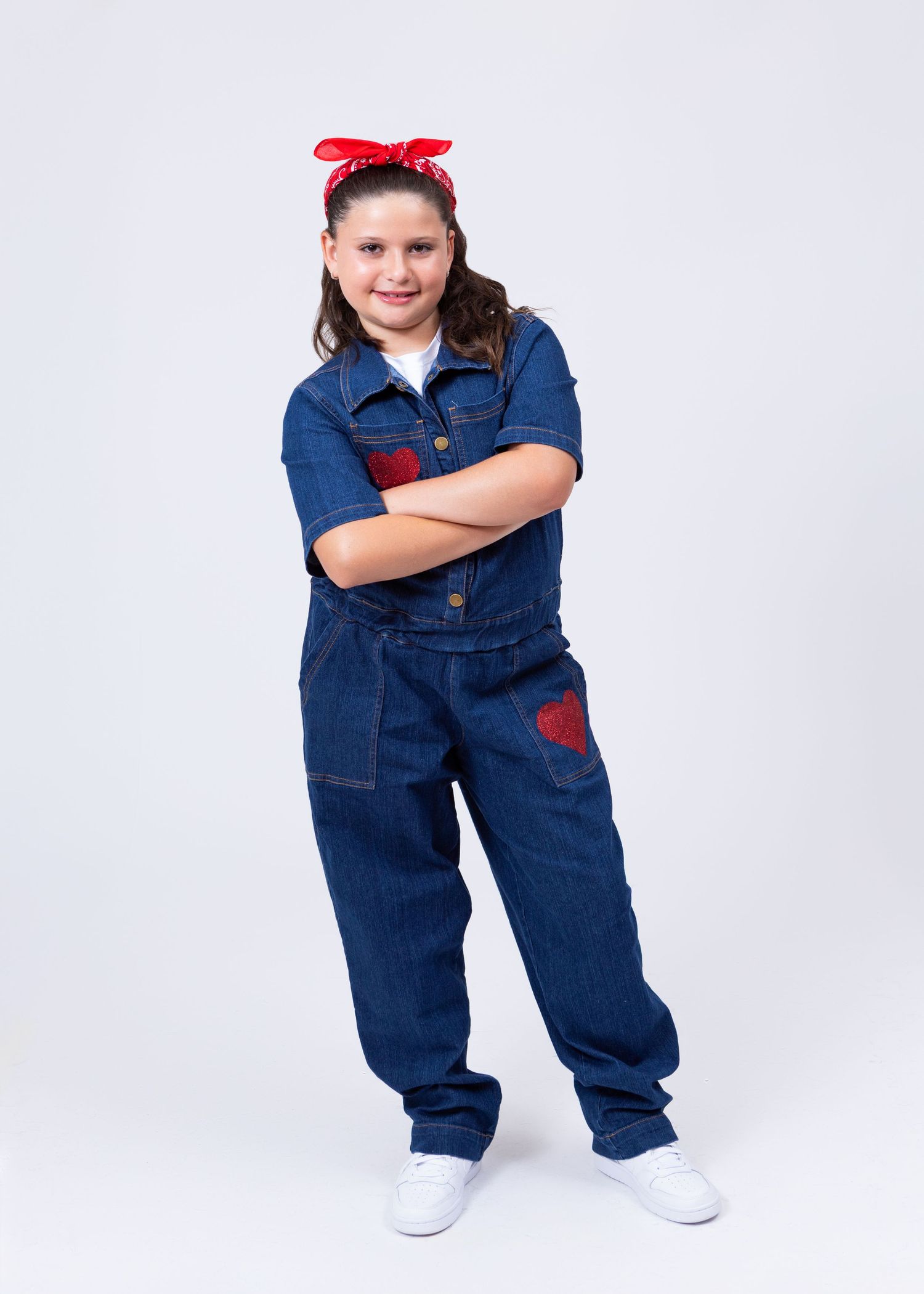 Girl in denim jumpsuit with red bandana headband poses with arms crossed in Rosie the Riveter costume.