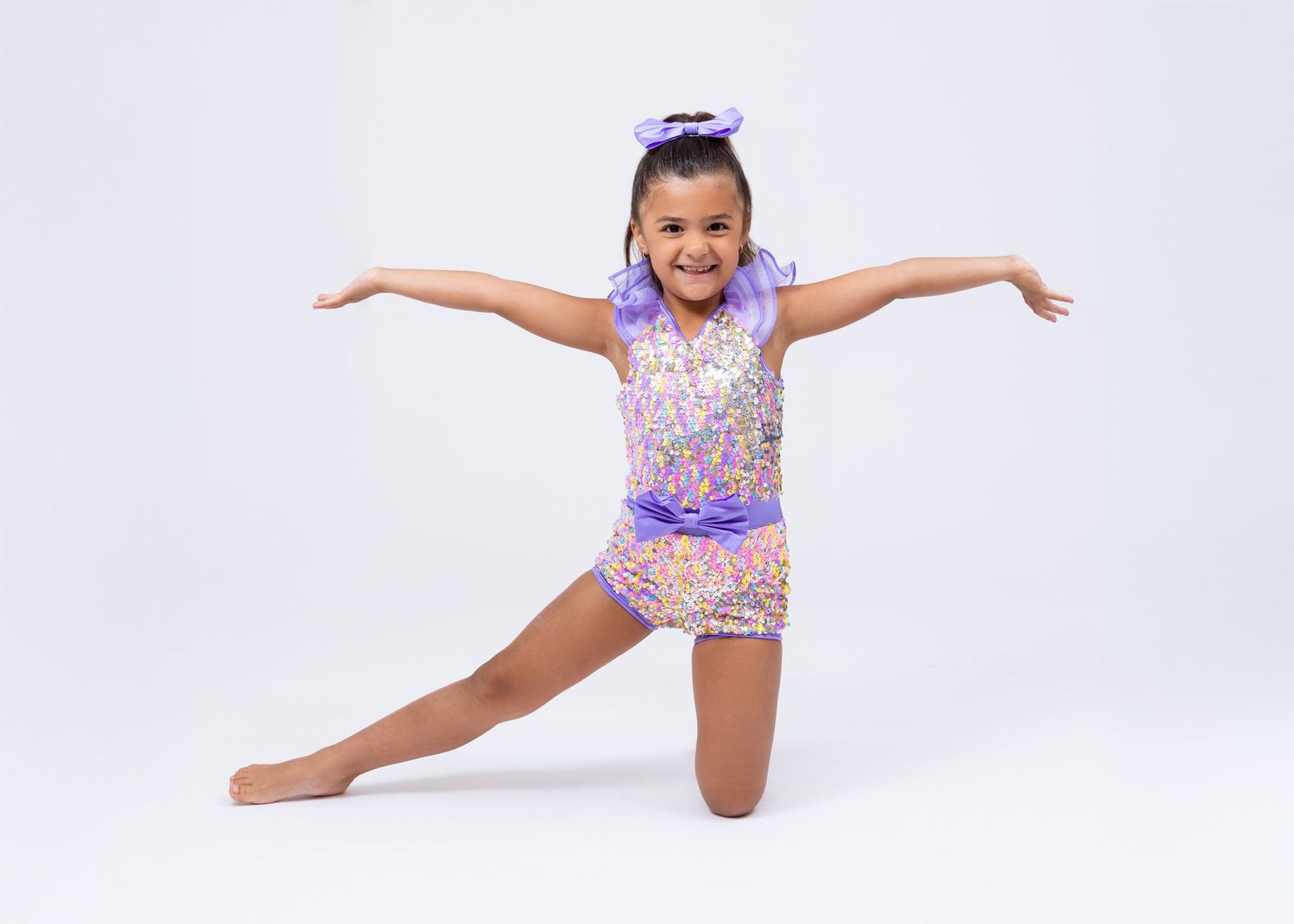 Young girl in purple sequined dance costume performing a split pose on white background.