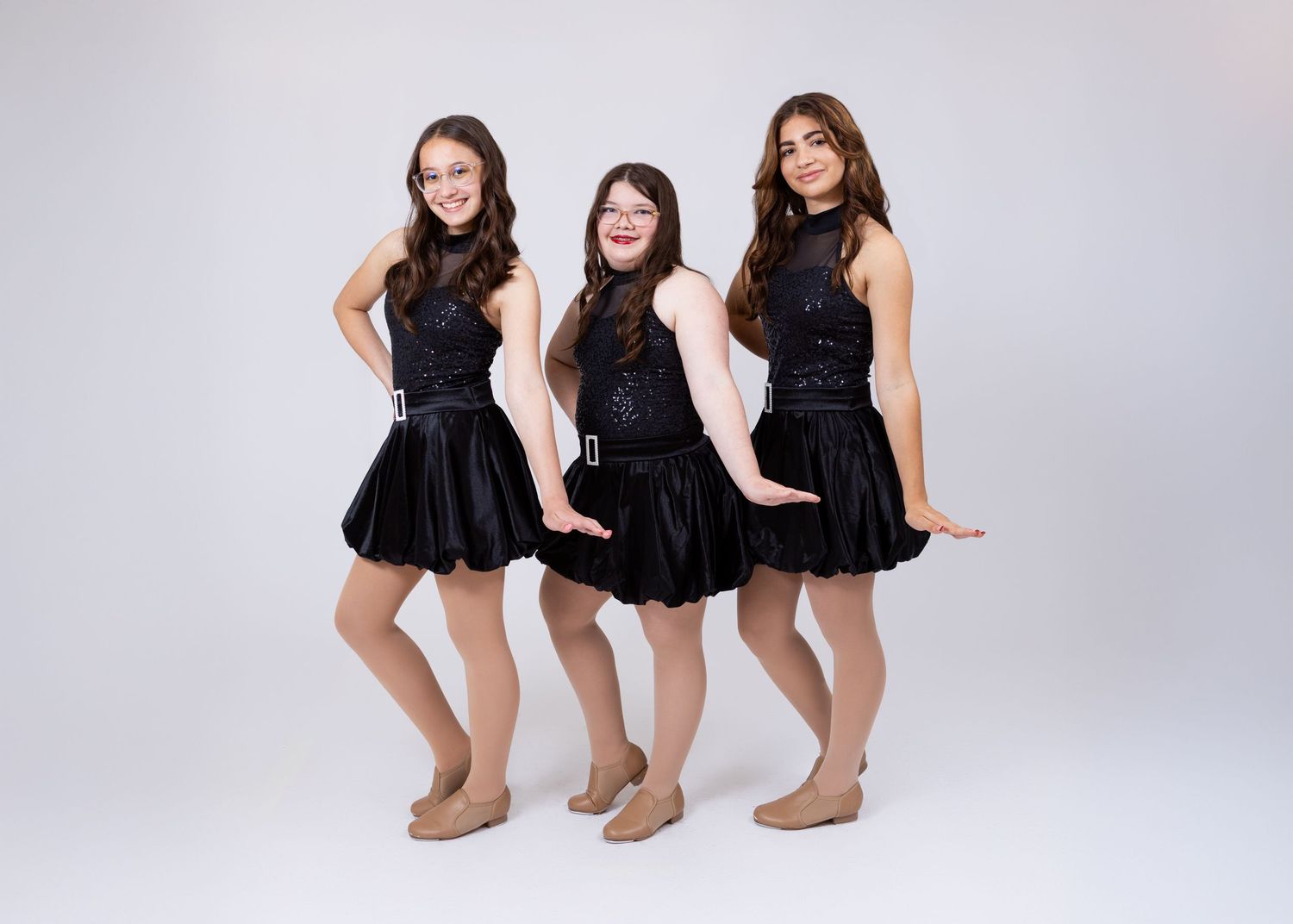 Three young dancers in black sequin dresses pose together in a dance studio portrait photo.