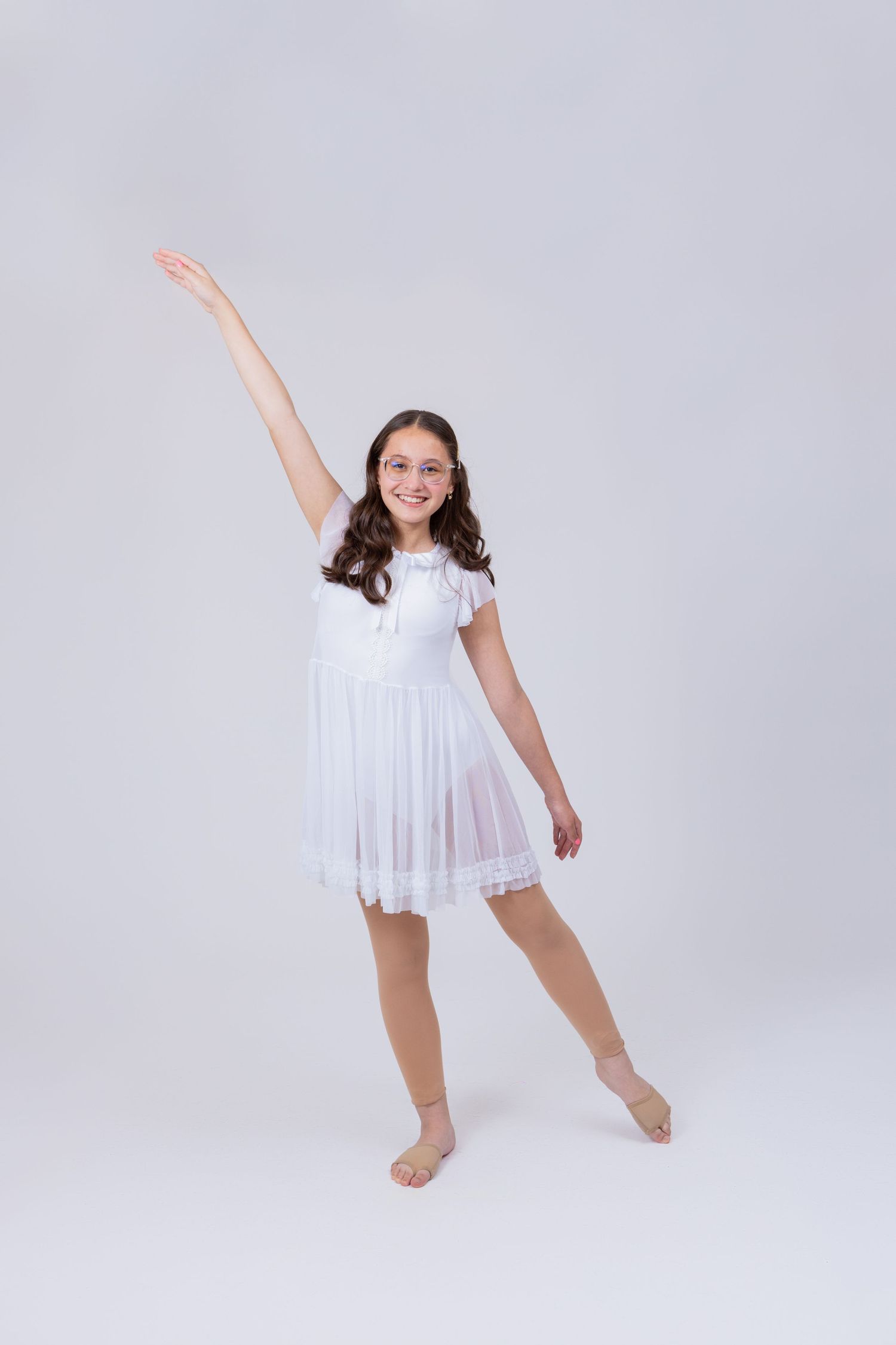 Teen girl in white lyrical dance dress raises one arm gracefully in ballet-inspired pose.