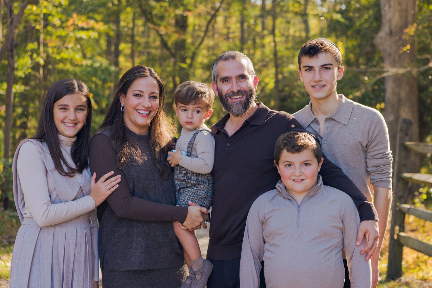 Happy family of six posing together outdoors with lush green trees in the background.