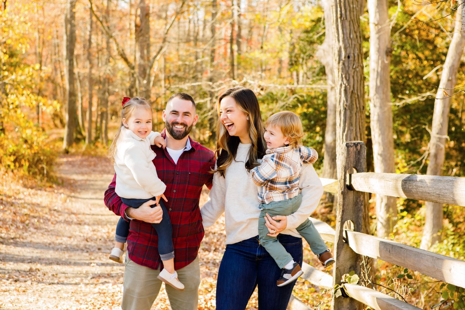 Happy family of four posing on a sunny autumn trail surrounded by golden fall foliage.
