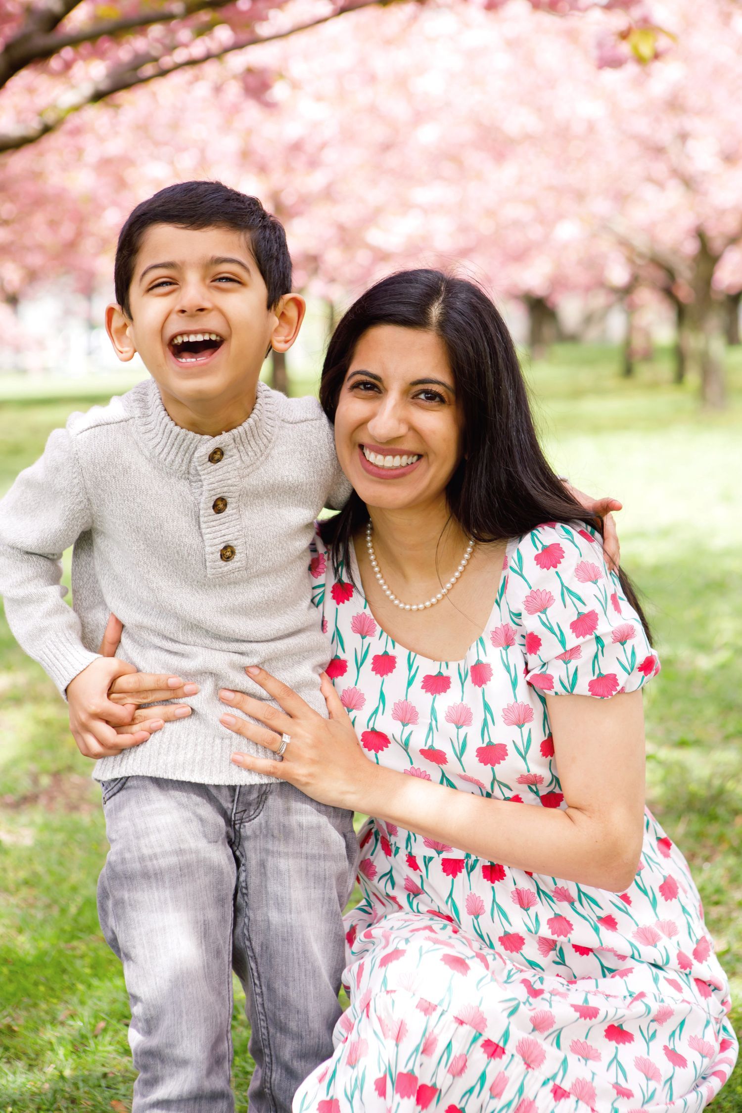 A joyful mother and son laughing together under pink cherry blossom trees in a park during spring.