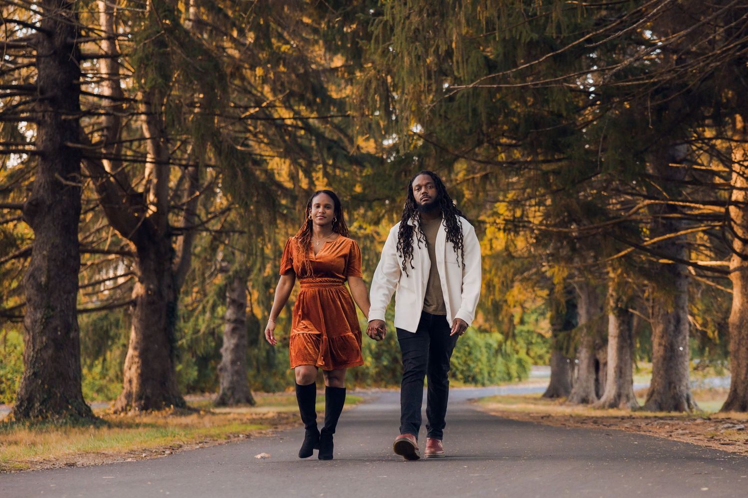 Couple holding hands walking down a tree-lined path during autumn season in a scenic park.