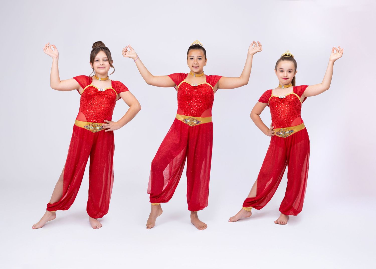 Three girls in red Arabian dance costumes with gold accents perform coordinated pose together.