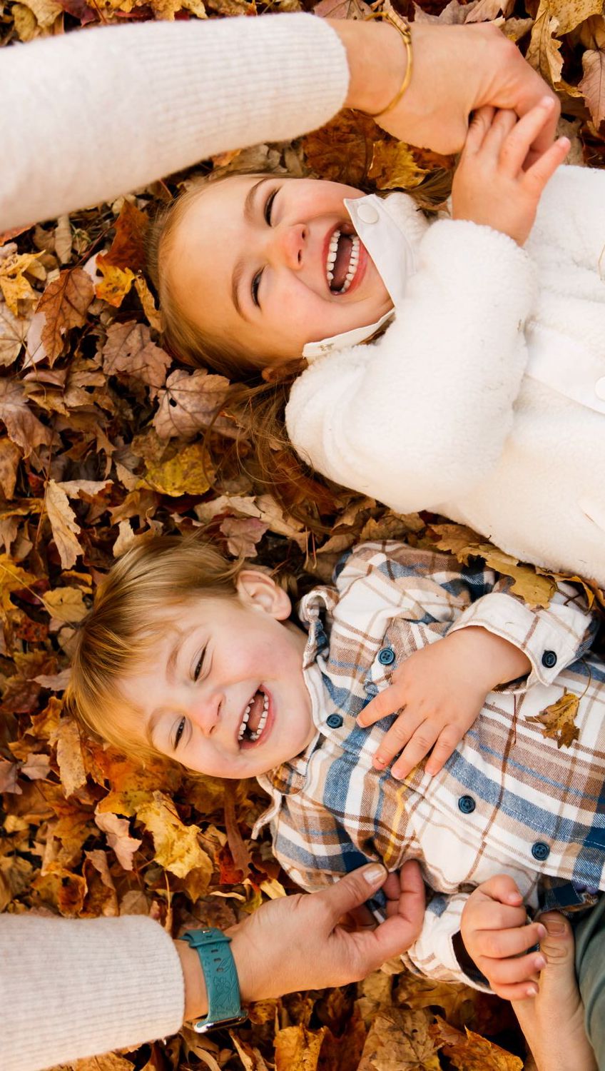 Mother and young child laughing joyfully while lying in autumn leaves together.