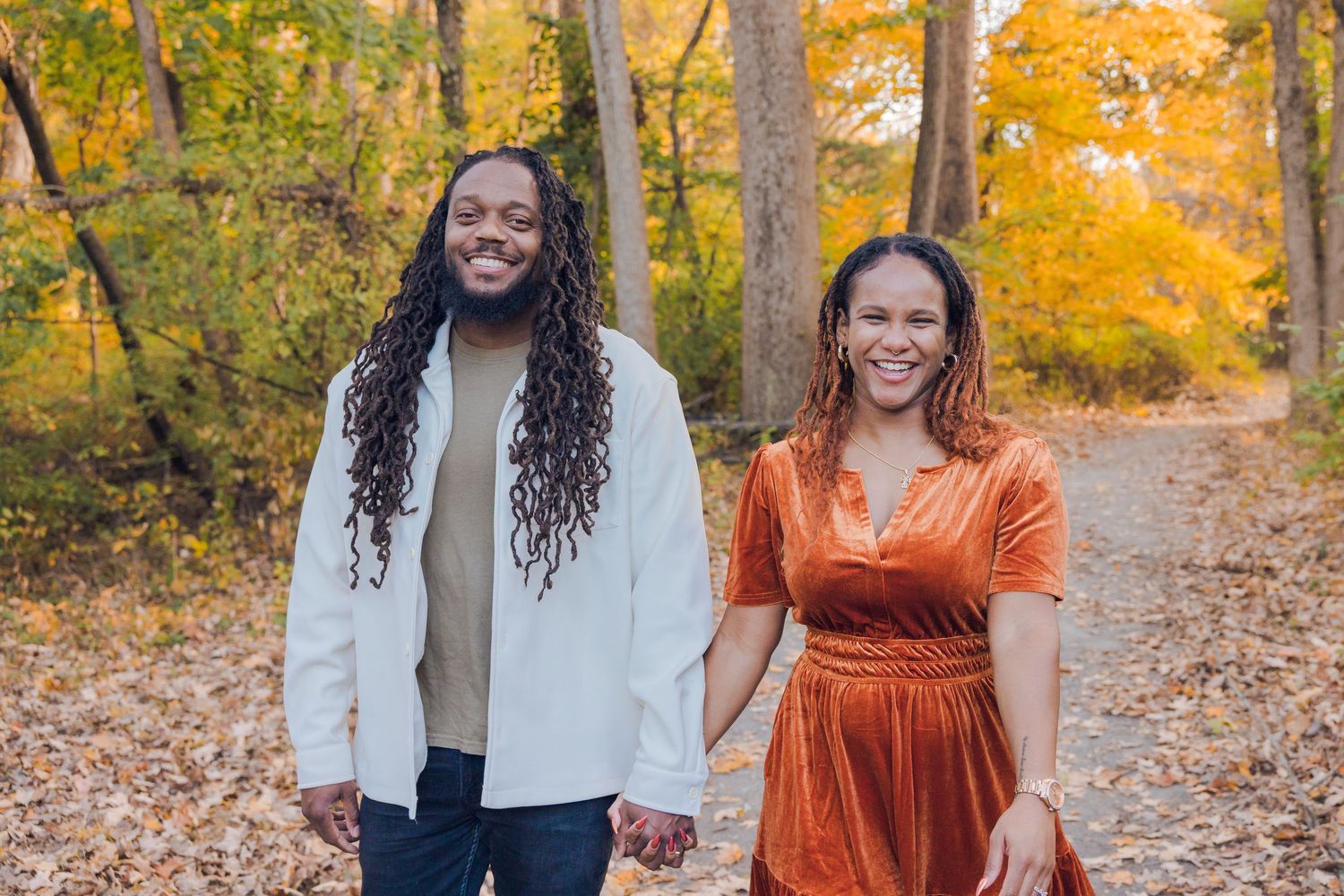 Smiling couple holding hands walking through a colorful autumn forest path with golden foliage.