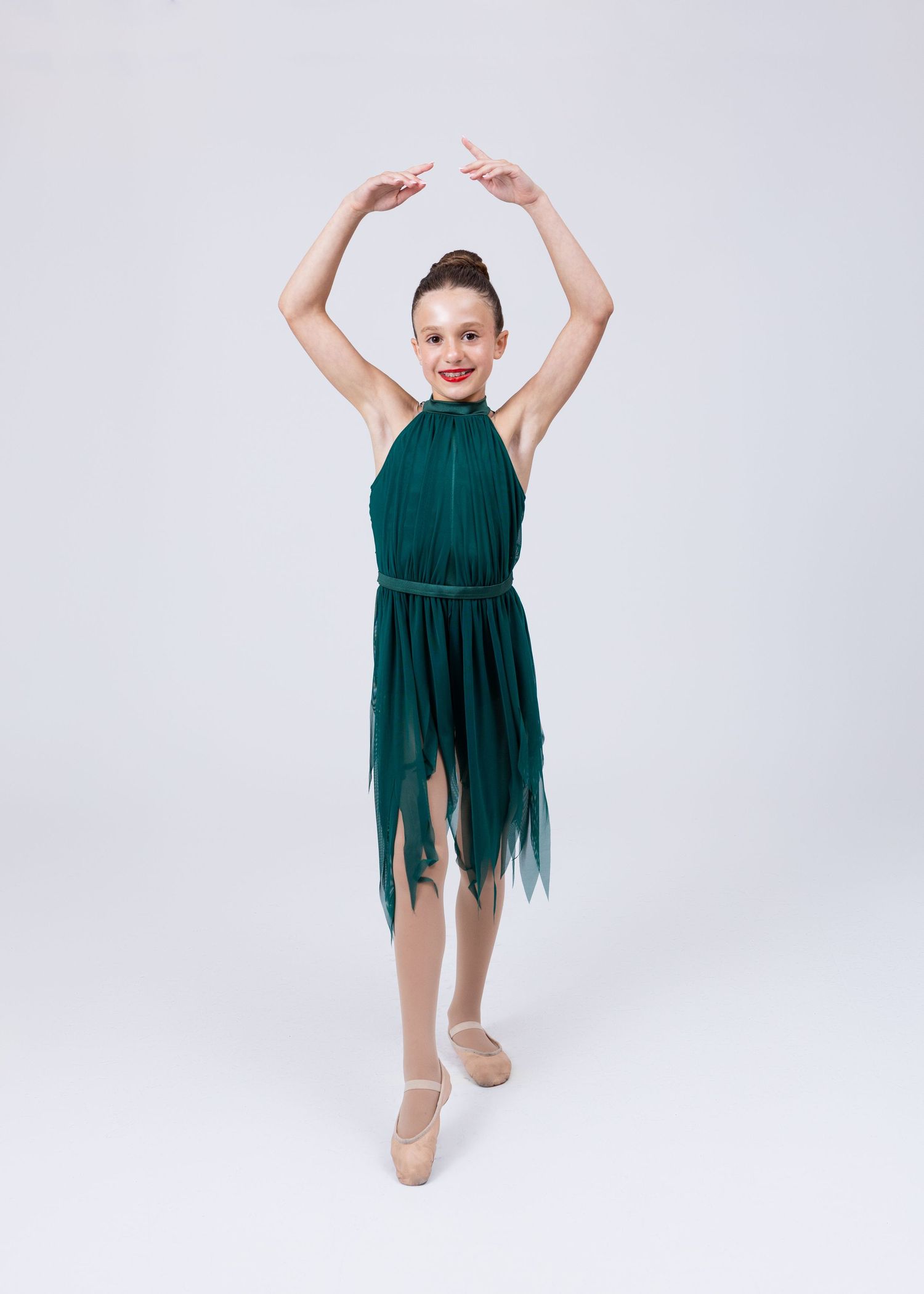 Young girl in emerald green halter dance dress with asymmetrical hem poses in ballet position.