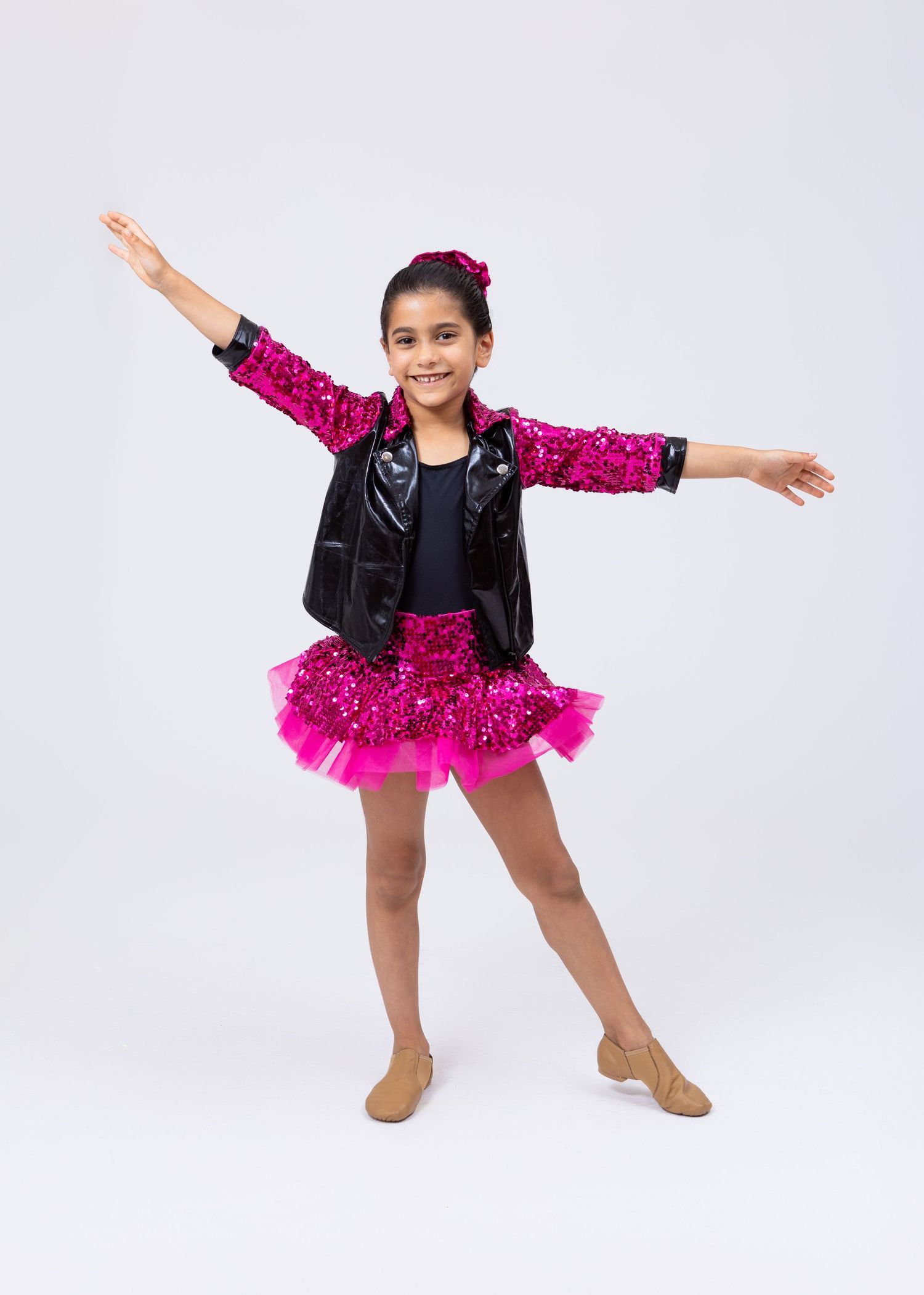 Young girl in pink sequin tutu and black leather jacket performs jazz dance pose.