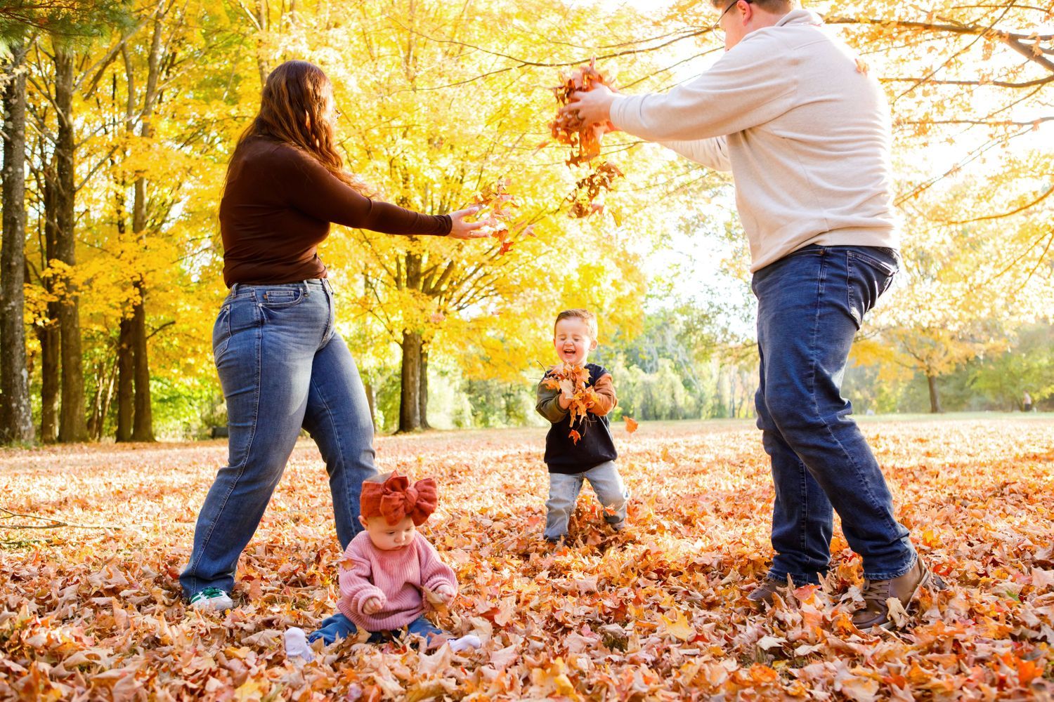 Family playing with fall leaves in colorful autumn park setting.