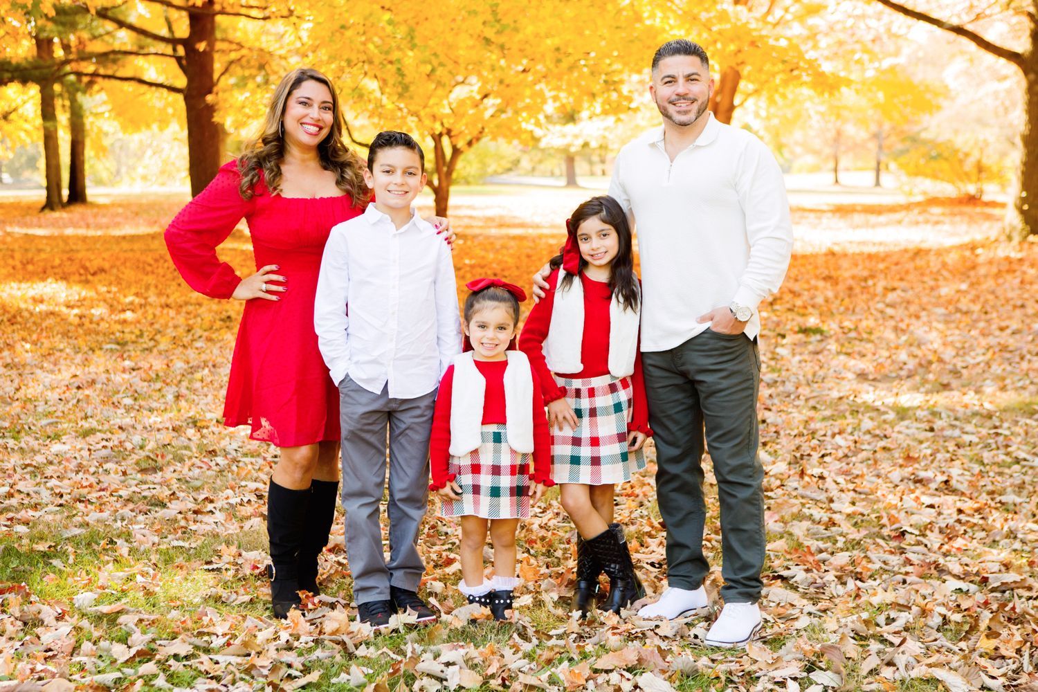 Family of five posing in red and plaid outfits among colorful fall foliage.
