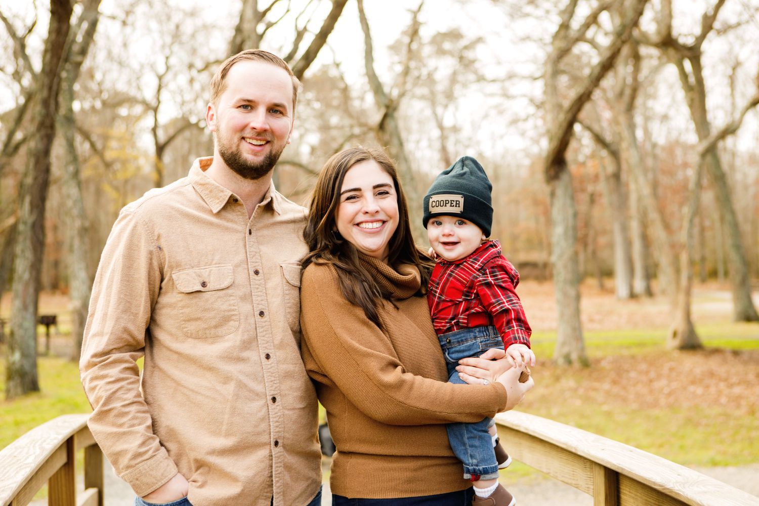 Young couple with baby on wooden bridge surrounded by fall trees.