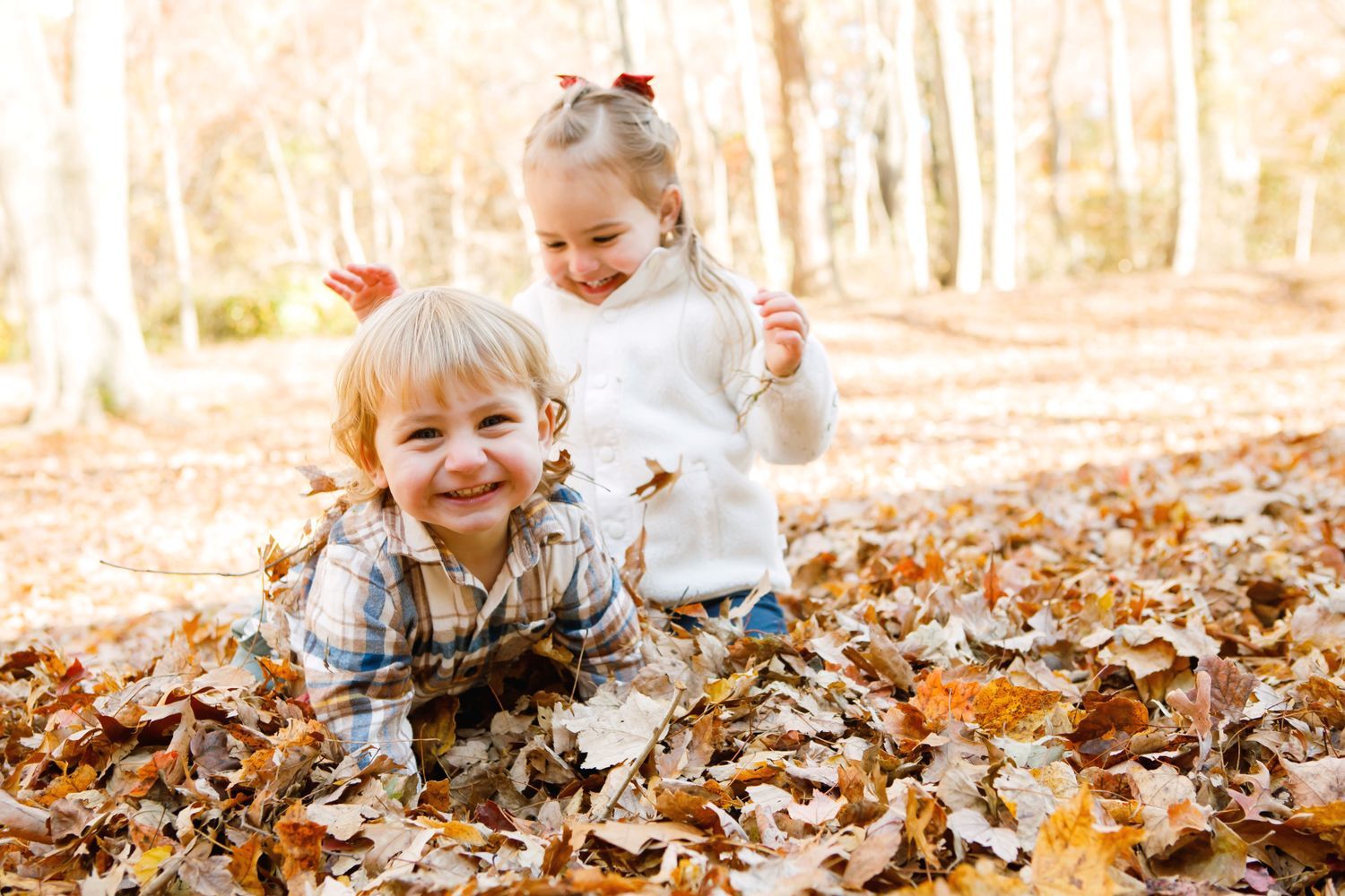 Two young children laughing and playing in a pile of autumn leaves outdoors.
