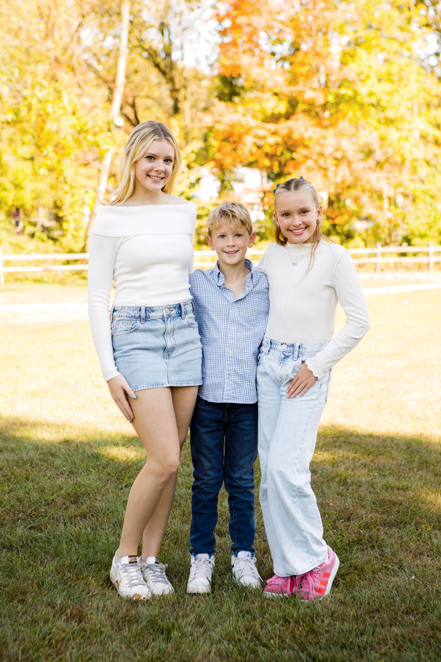 Teen girl, young boy, and preteen girl posing together on a sunny autumn lawn.